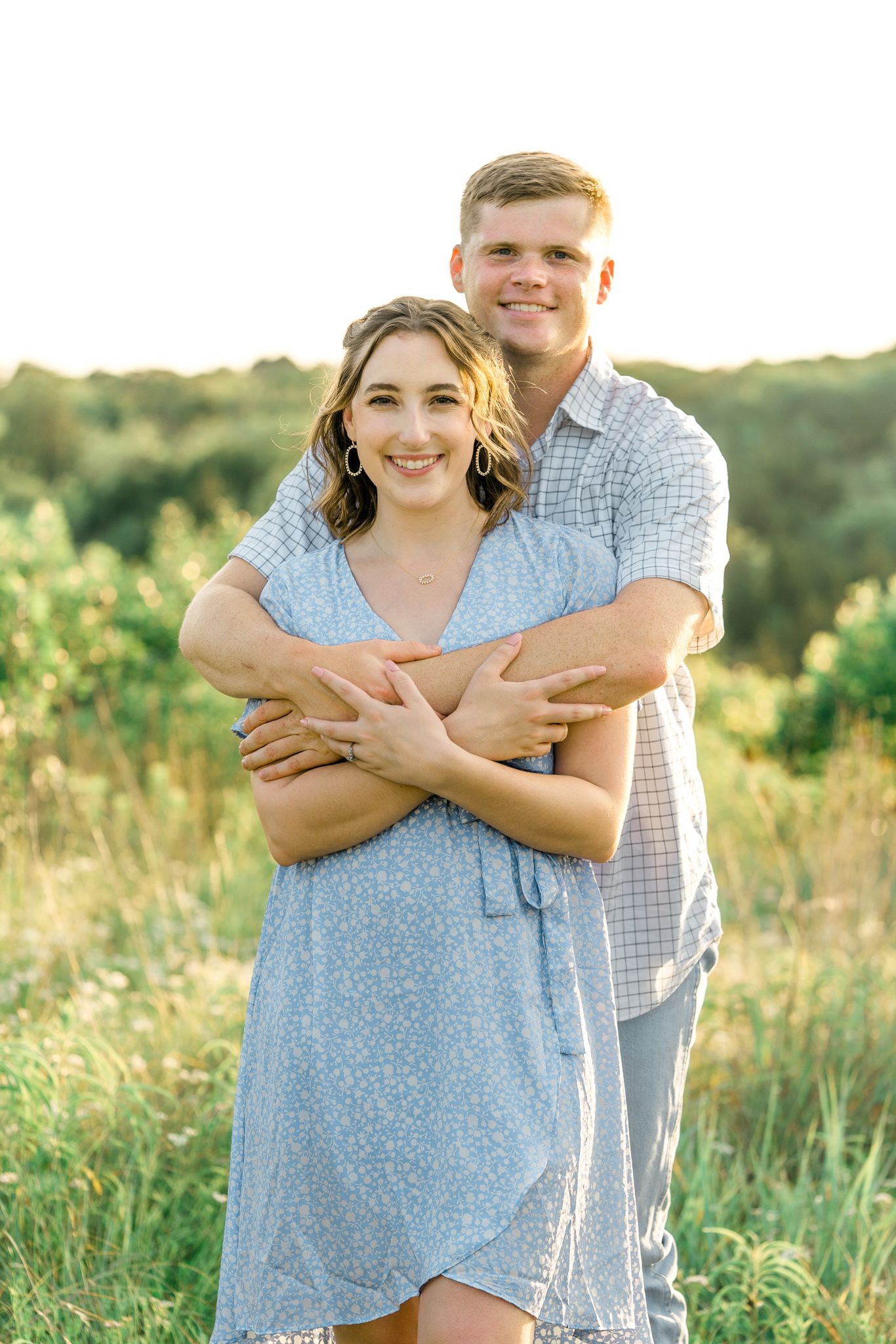 A joyful couple in blue clothing embraces while laughing in a sunlit summer field.