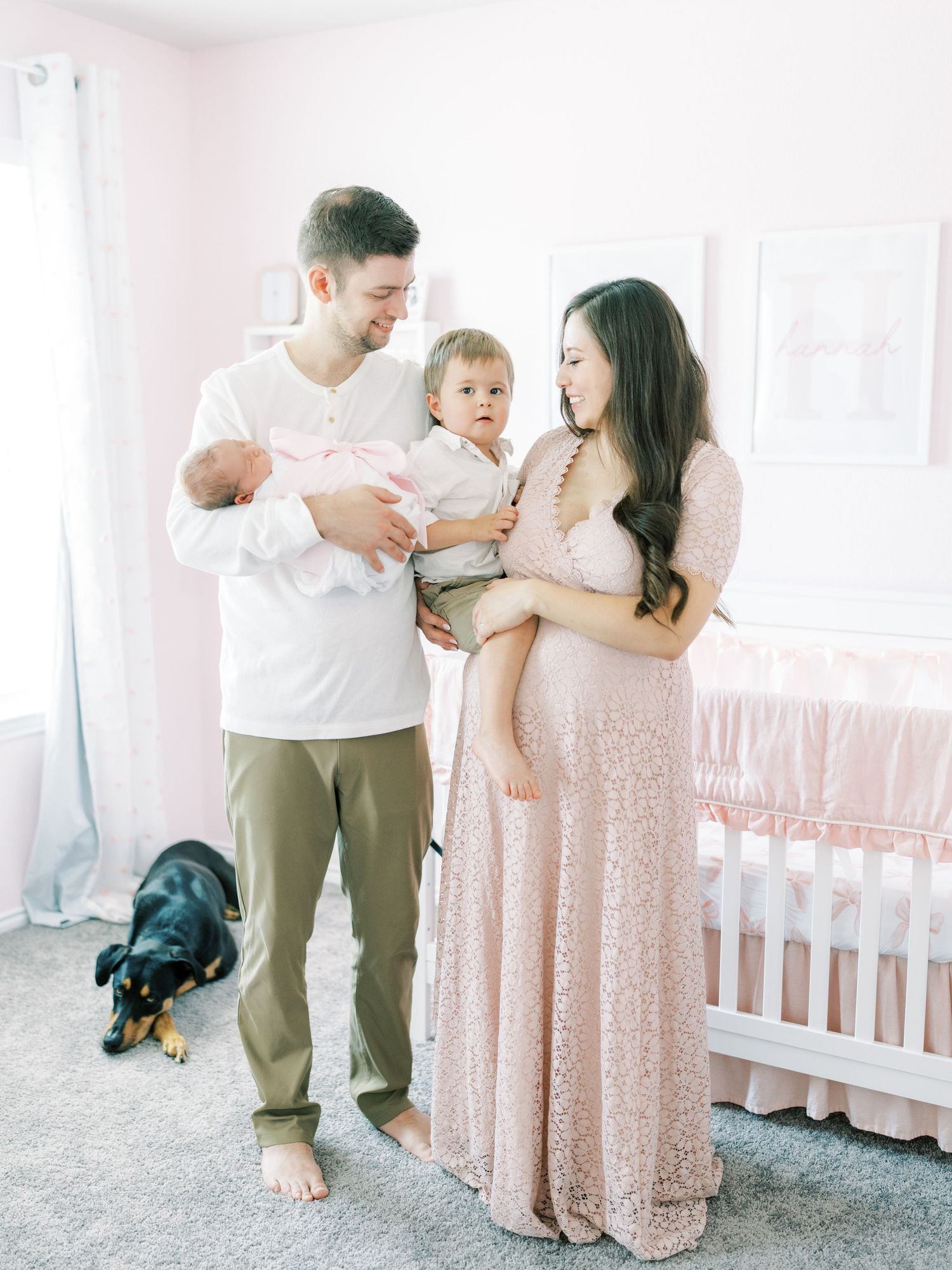 Family members share tender moments in a nursery with white decor and pink accents during an intimate photo session.