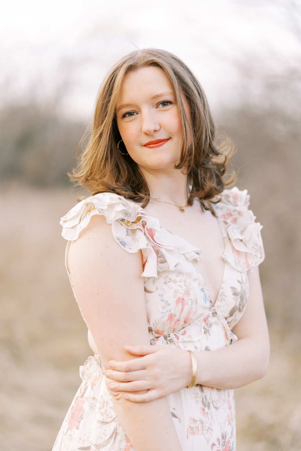 A person in a floral ruffled dress poses outdoors in soft, dreamy lighting during a portrait session.