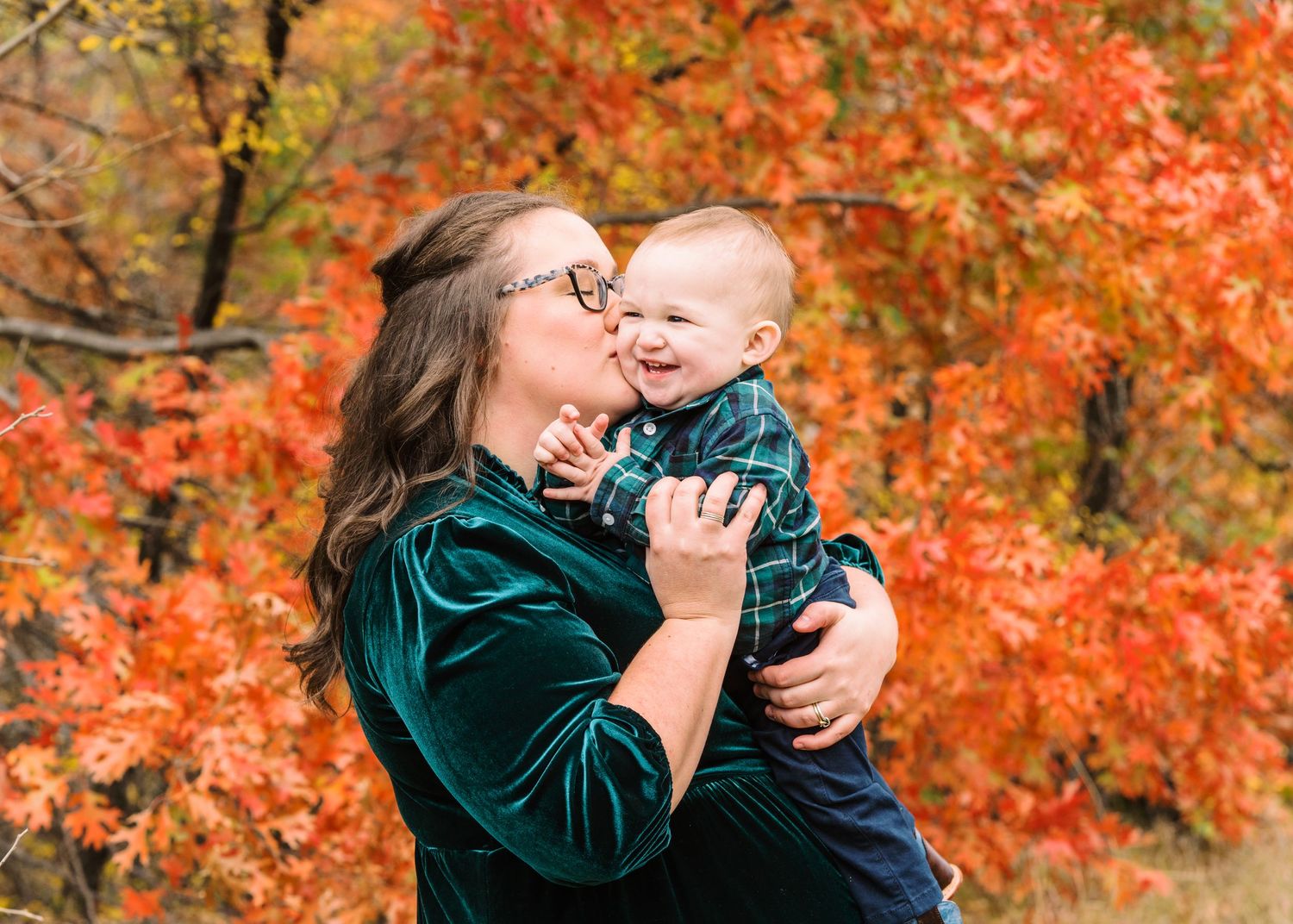 A tender autumn moment with a velvet green dress against vibrant orange fall foliage.