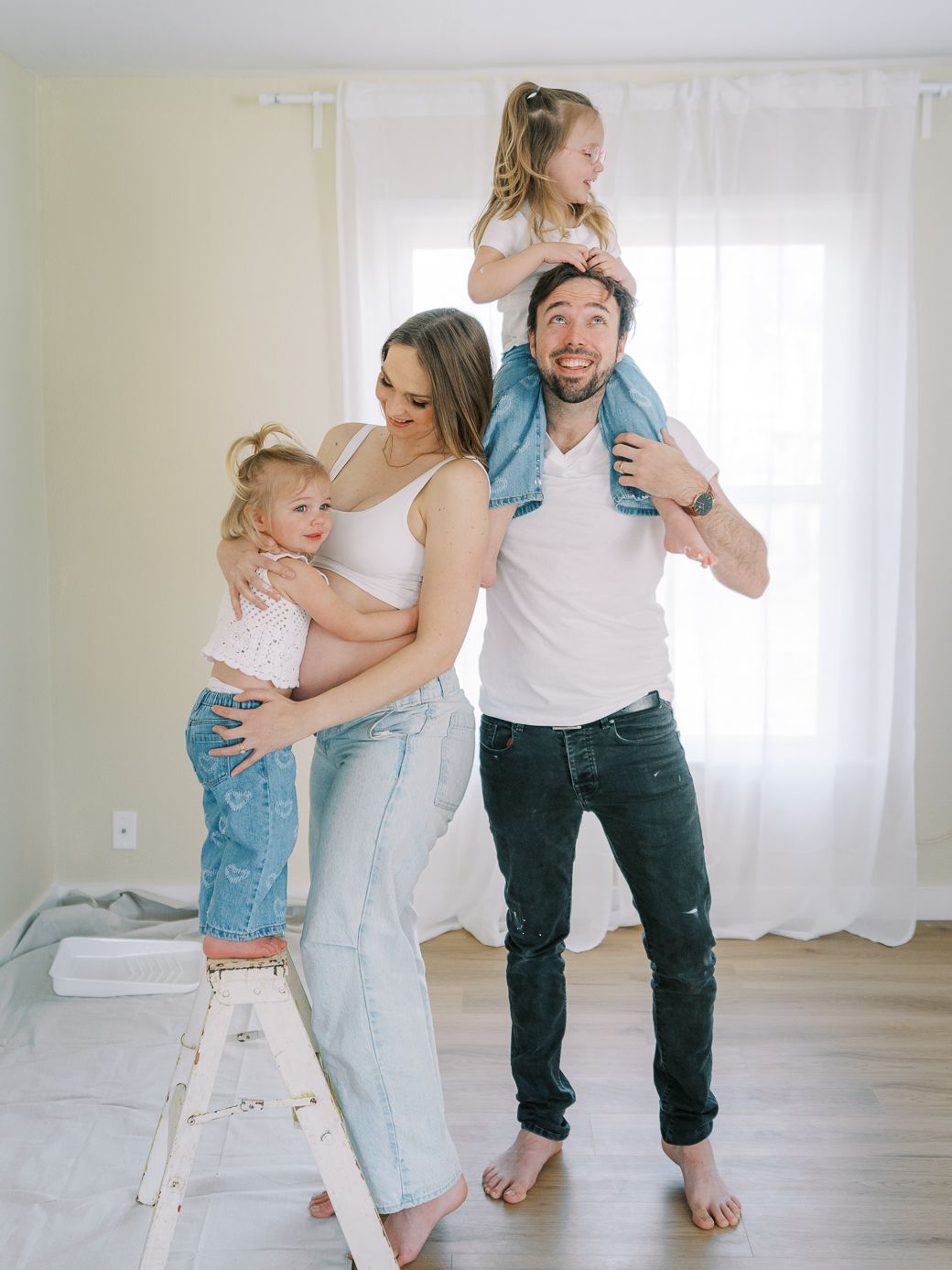 Family in matching white tops and denim playing together in a bright minimalist room.