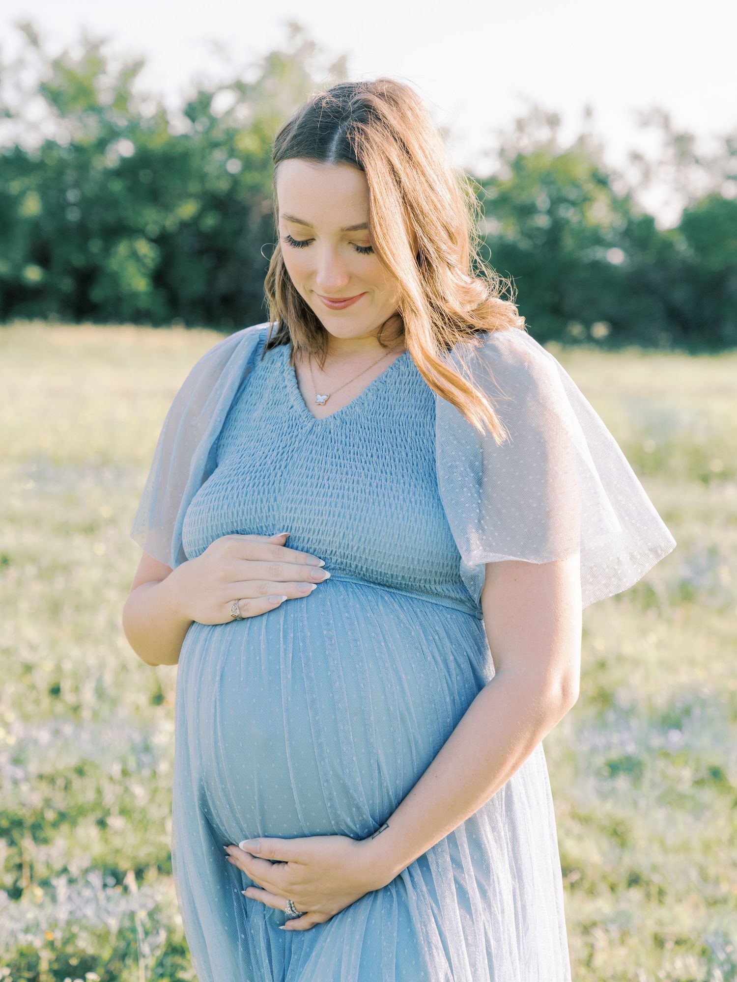 A series of maternity photos showing a woman in a blue dress cradling her baby bump in a sunny meadow.