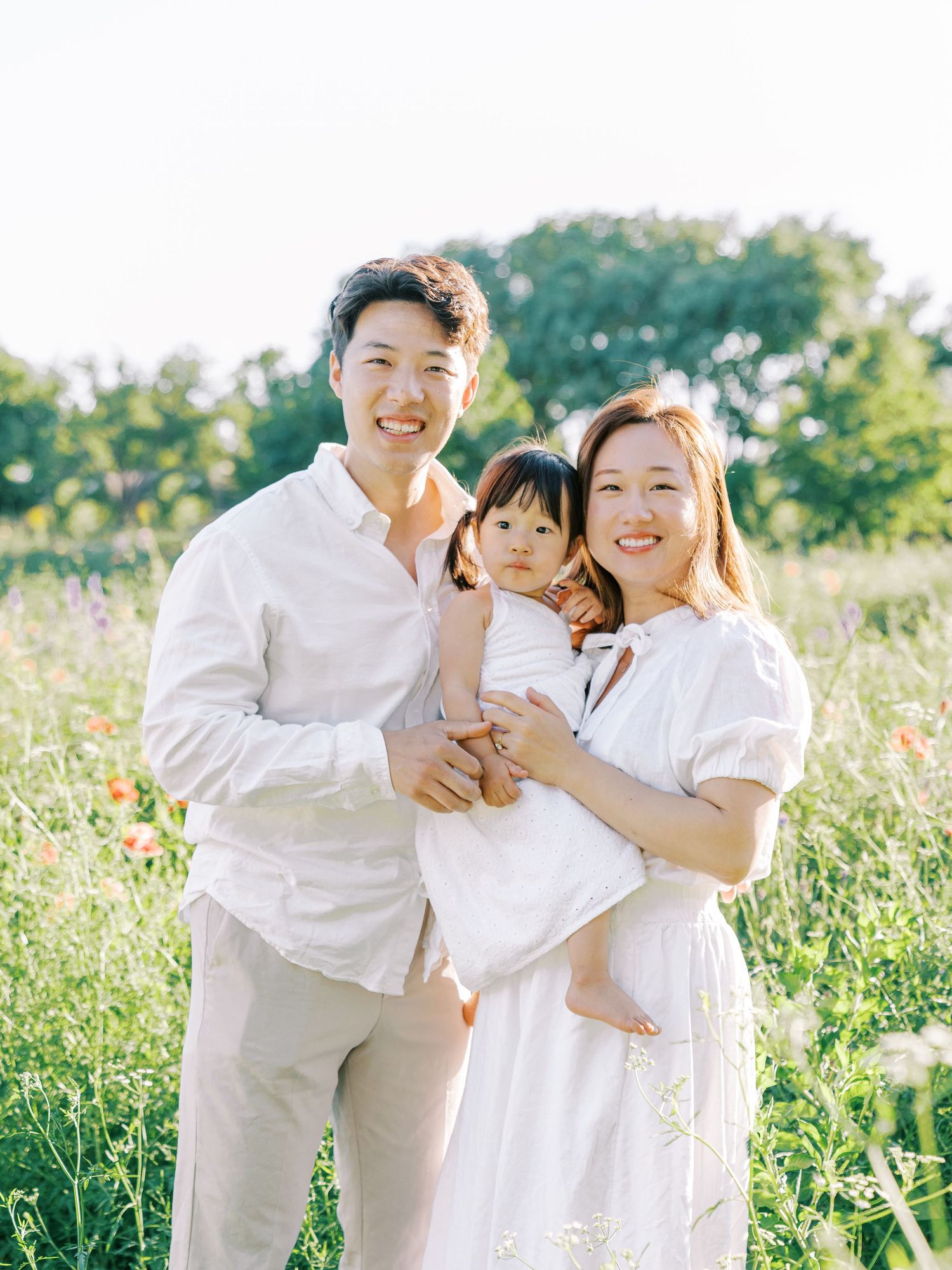 A family shares joyful moments together in a sunlit meadow wearing coordinated white outfits.