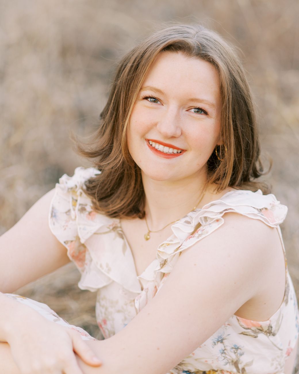 Portrait photograph in soft lighting featuring floral dress and natural outdoor setting at sunset.