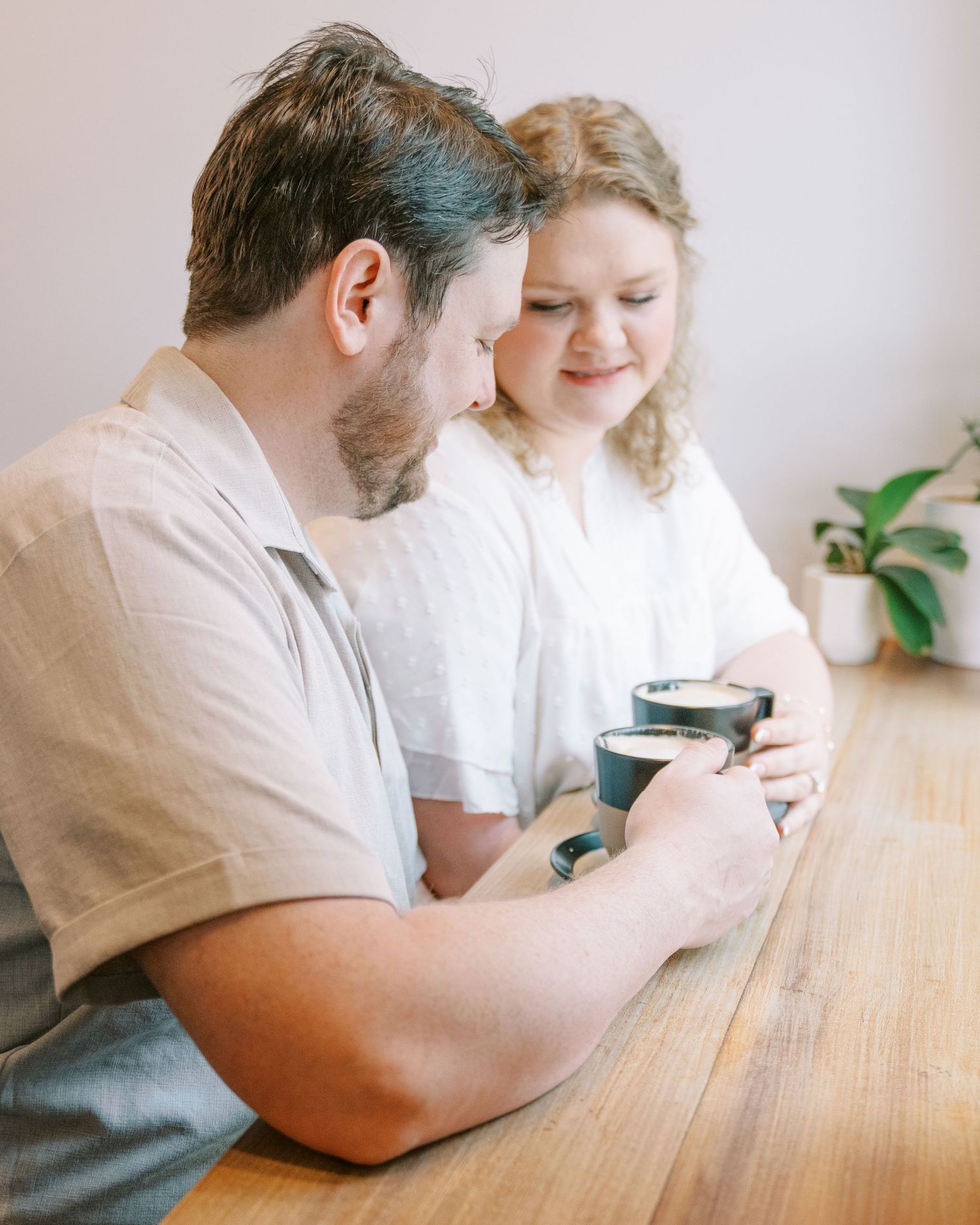 Couple sharing coffee at a wooden table, smiling and enjoying a cozy moment together indoors.