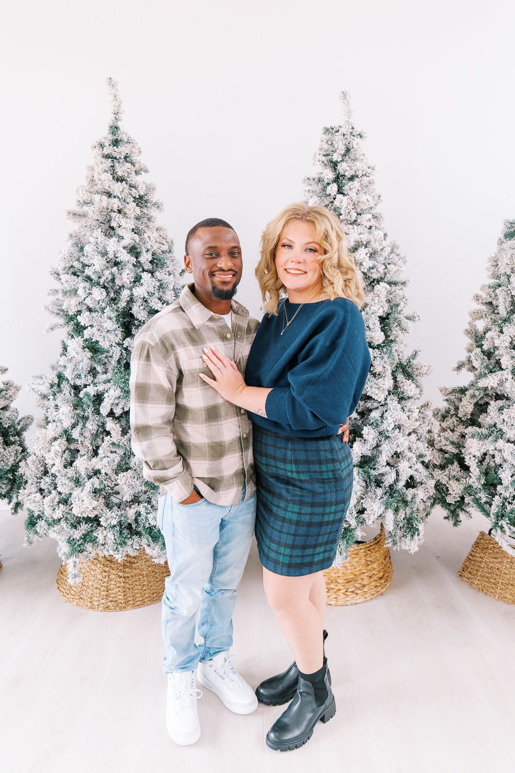 A couple dances and poses together in front of white flocked Christmas trees during a holiday photoshoot.