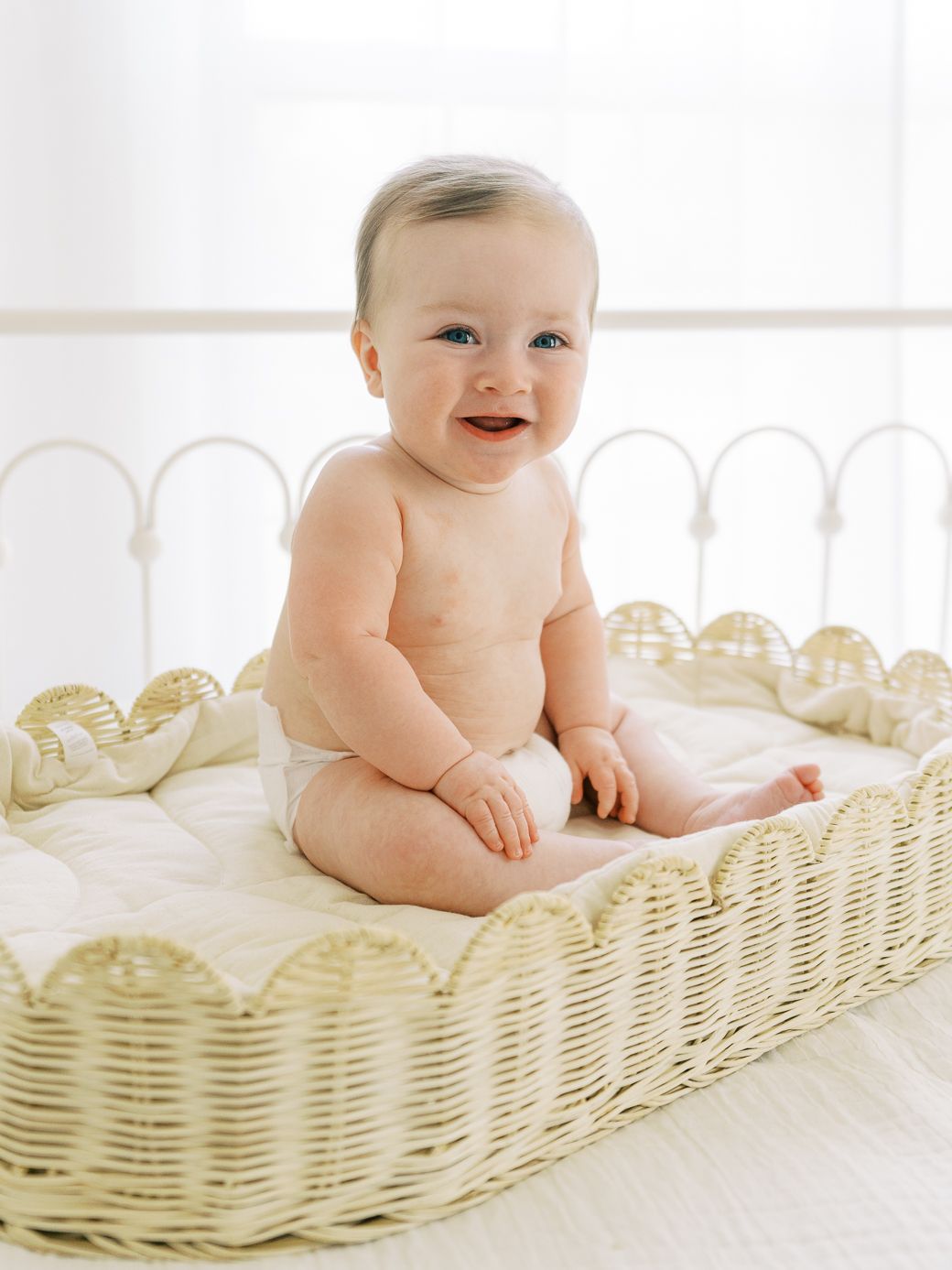 Smiling baby lying in white wicker bassinet on soft bedding.