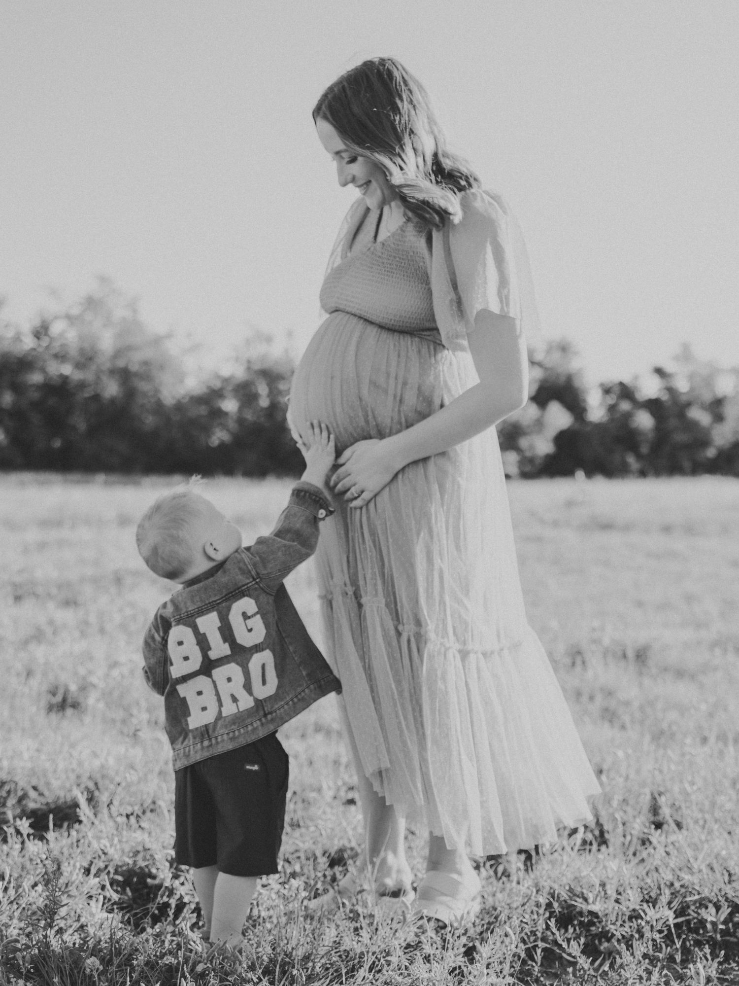 Black and white maternity family photos in a meadow with ultrasound pictures and flowing dress.