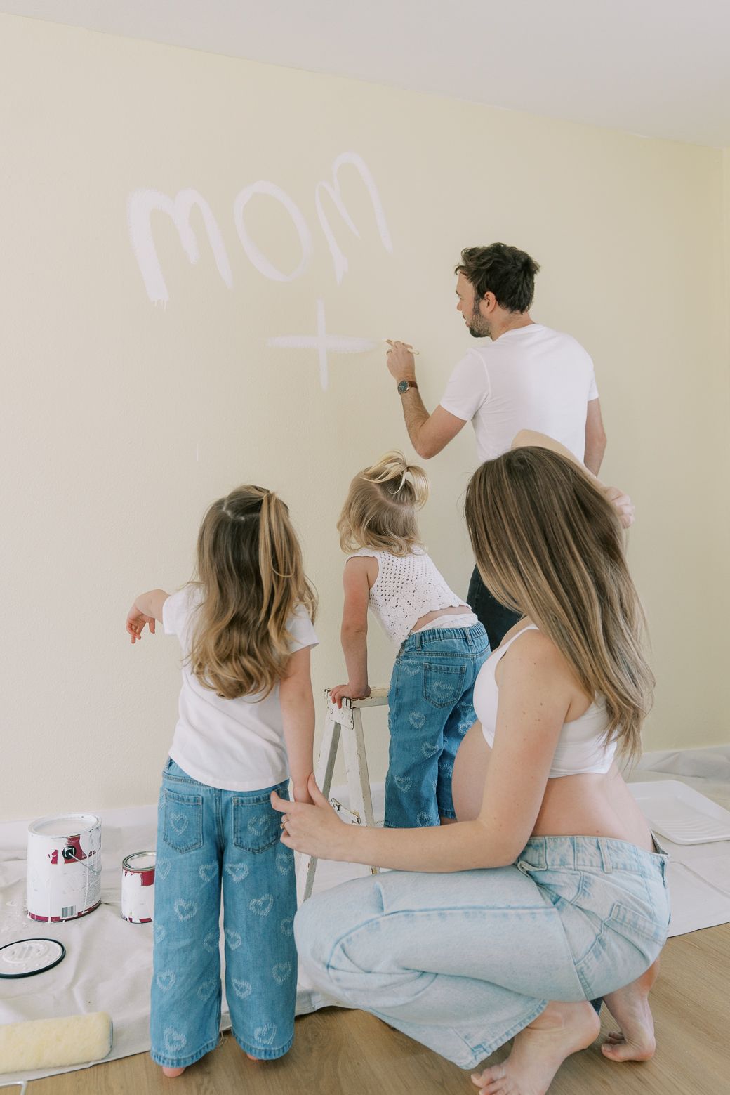 Family members paint a wall together in a bright empty room with natural lighting.