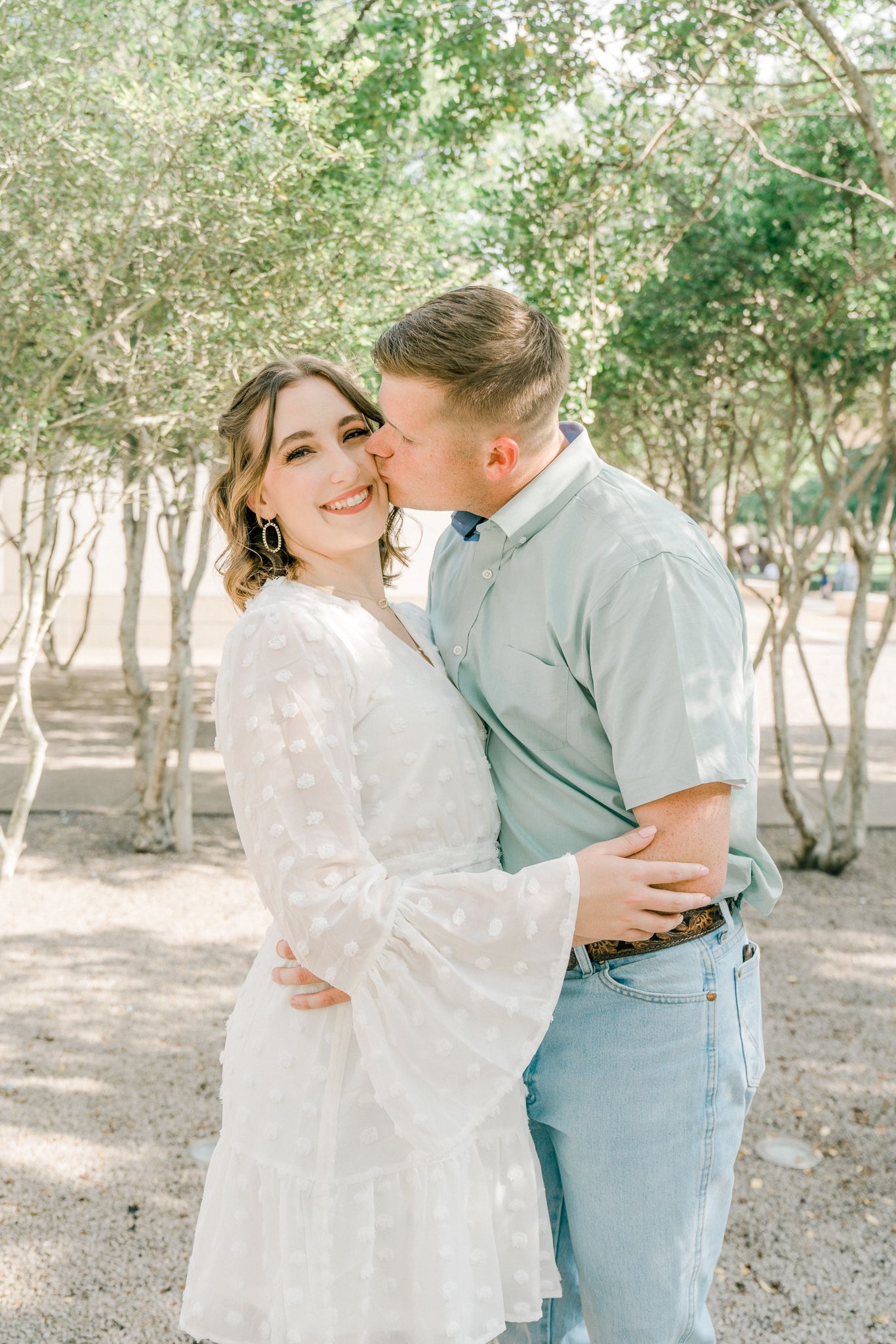 Romantic outdoor engagement photo session showing couple embracing among trees in natural light.