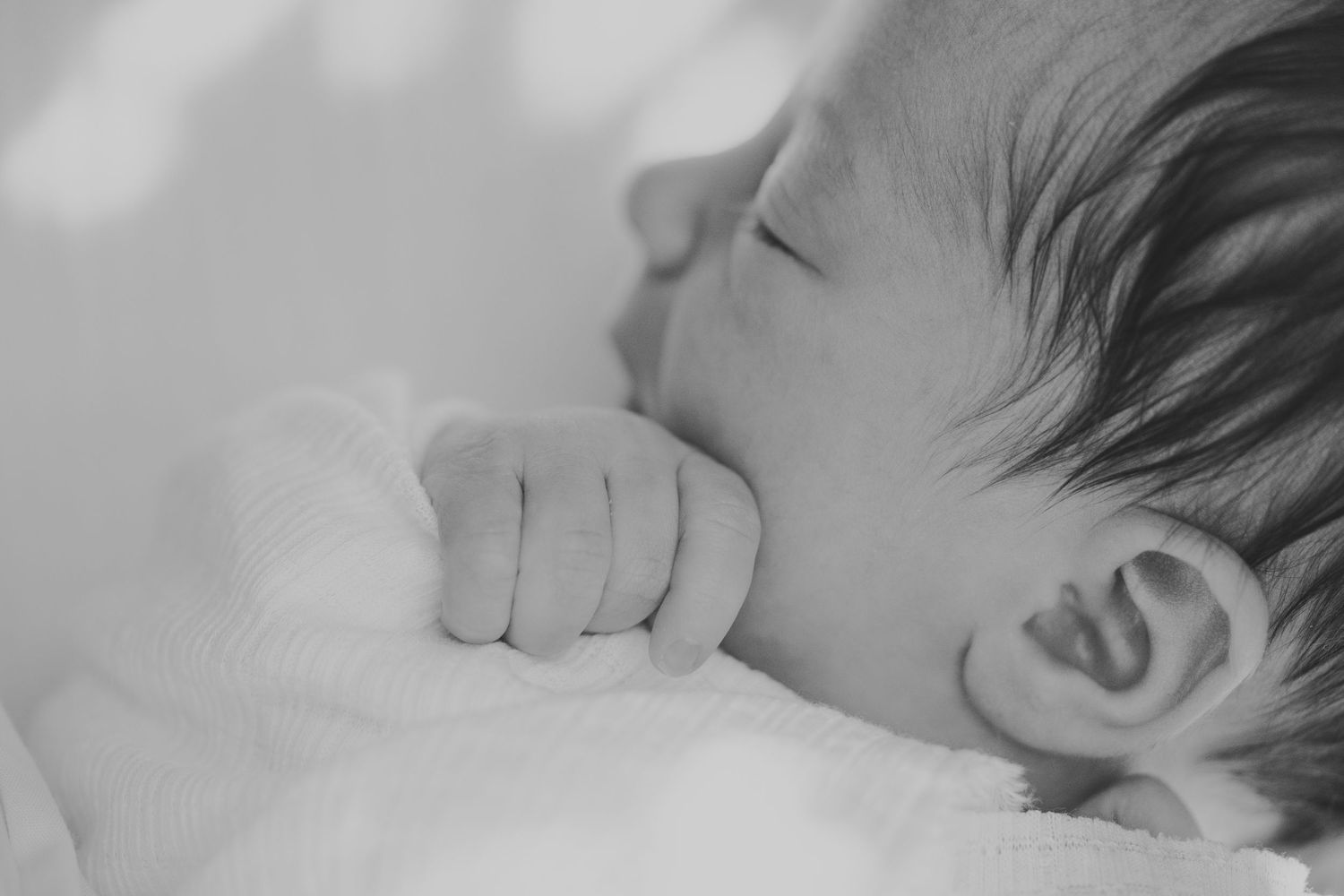 Close-up black and white photo of a sleeping baby with hand near mouth in peaceful slumber.