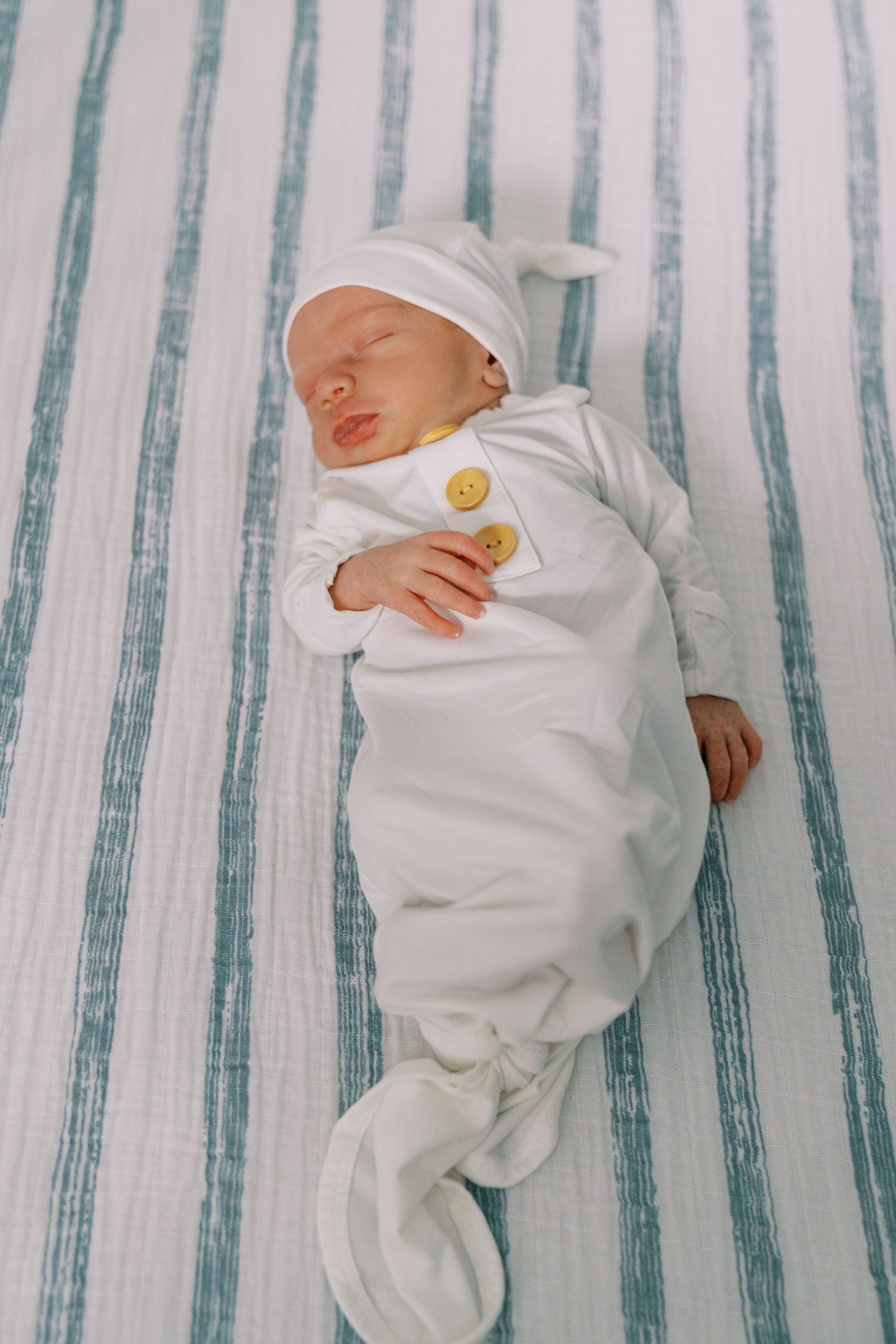 Sleeping newborn in white outfit and cap rests on striped bedding.