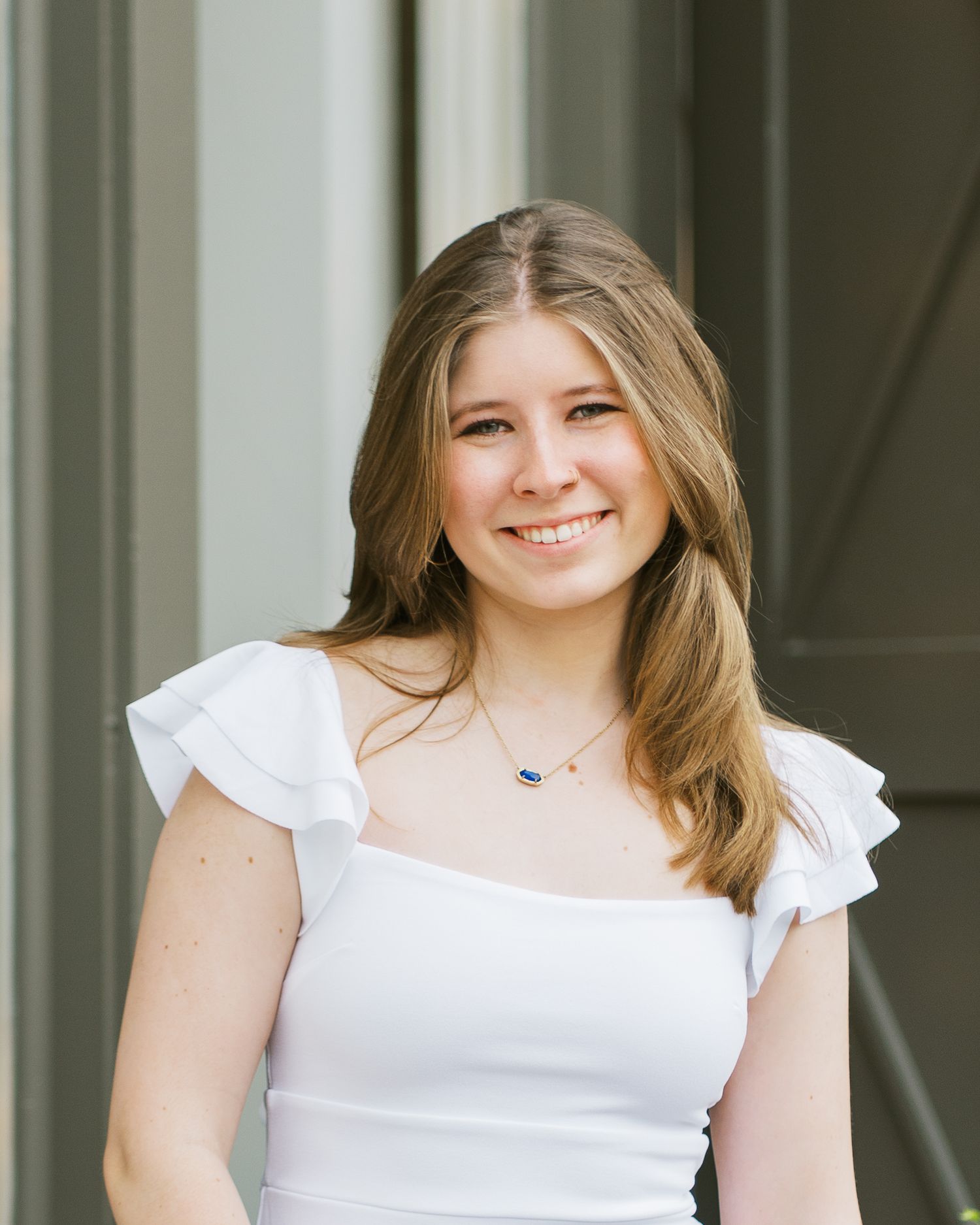Young woman in white ruffled top poses outdoors for a portrait session.
