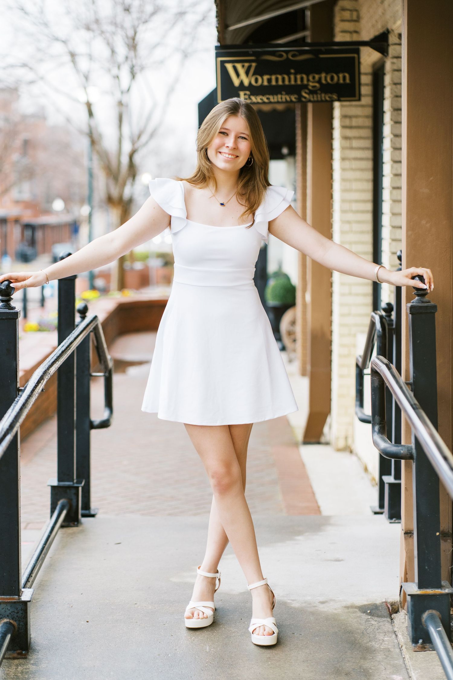 Person in white summer dress and sandals poses cheerfully on ramp outside Wormington business entrance.