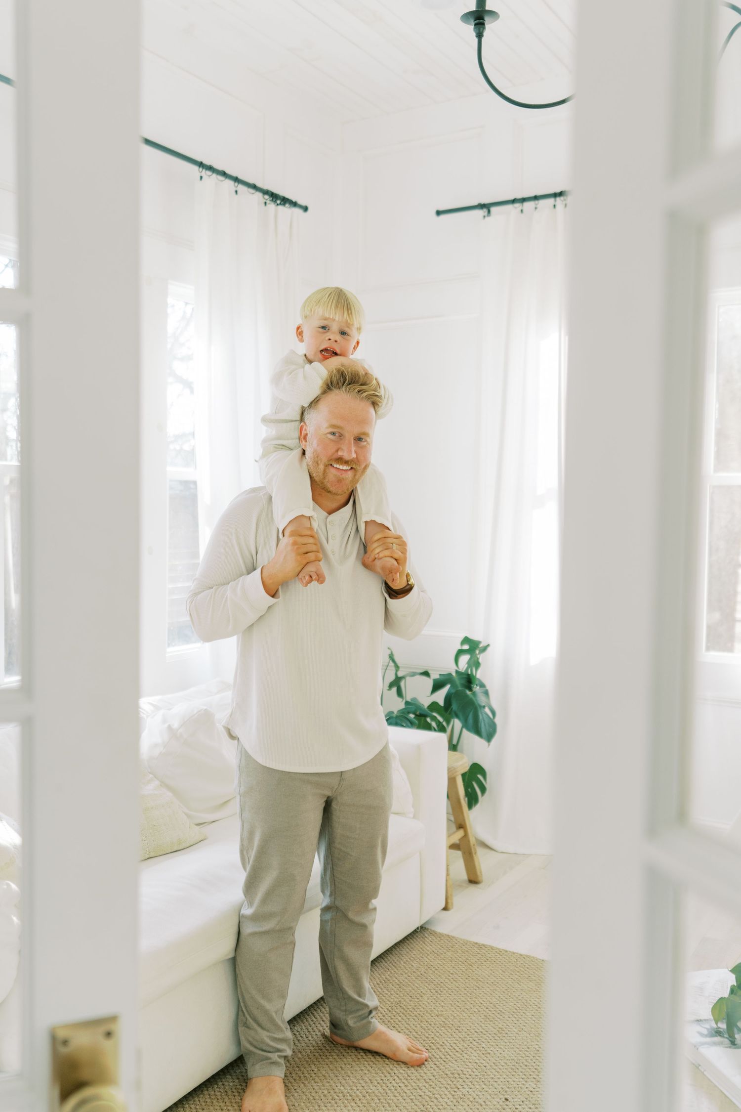 Playful family interactions captured in bright white room with minimal decor.