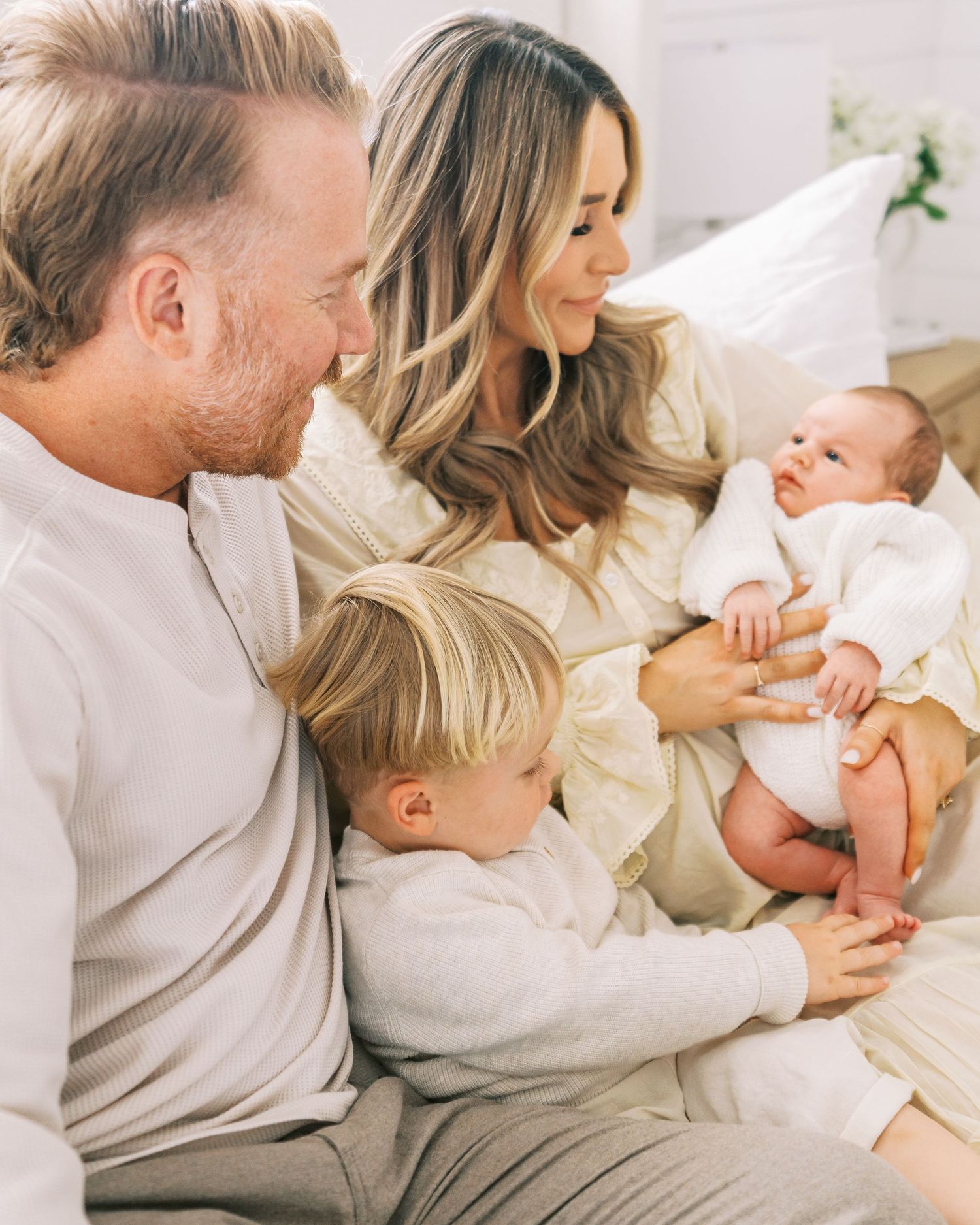 Family shares intimate moment together on couch wearing matching cream and grey outfits.