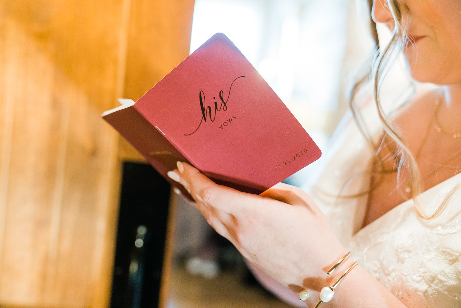 A person holds a small red book in their hands while sitting at a wooden table with a warm glowing background.
