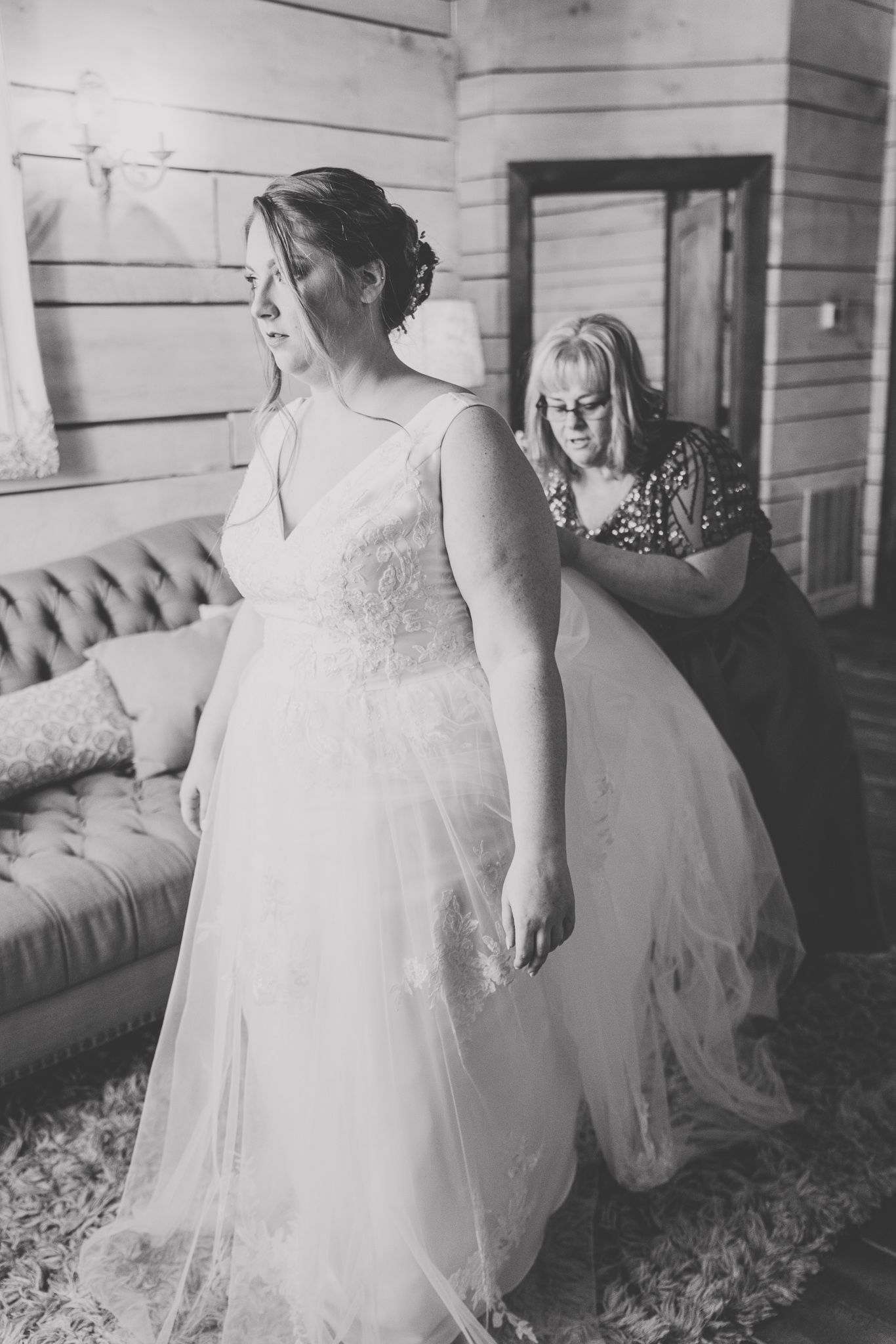 Black and white photo of final wedding dress adjustments being made in a vintage-style room.