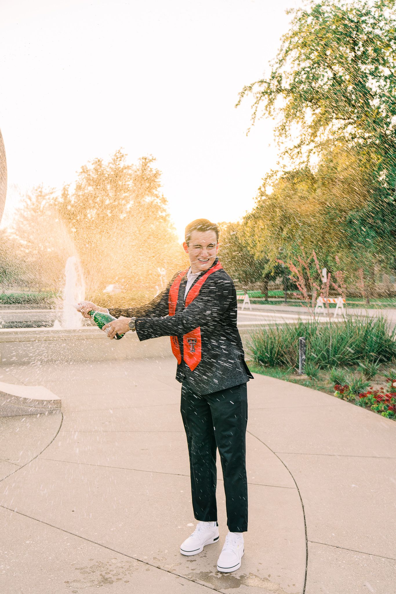 A person in black pants and orange safety vest stands on a concrete path during sunset.