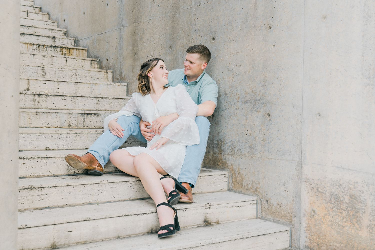 A romantic couple sits on outdoor concrete steps in a casual summer photoshoot setting.