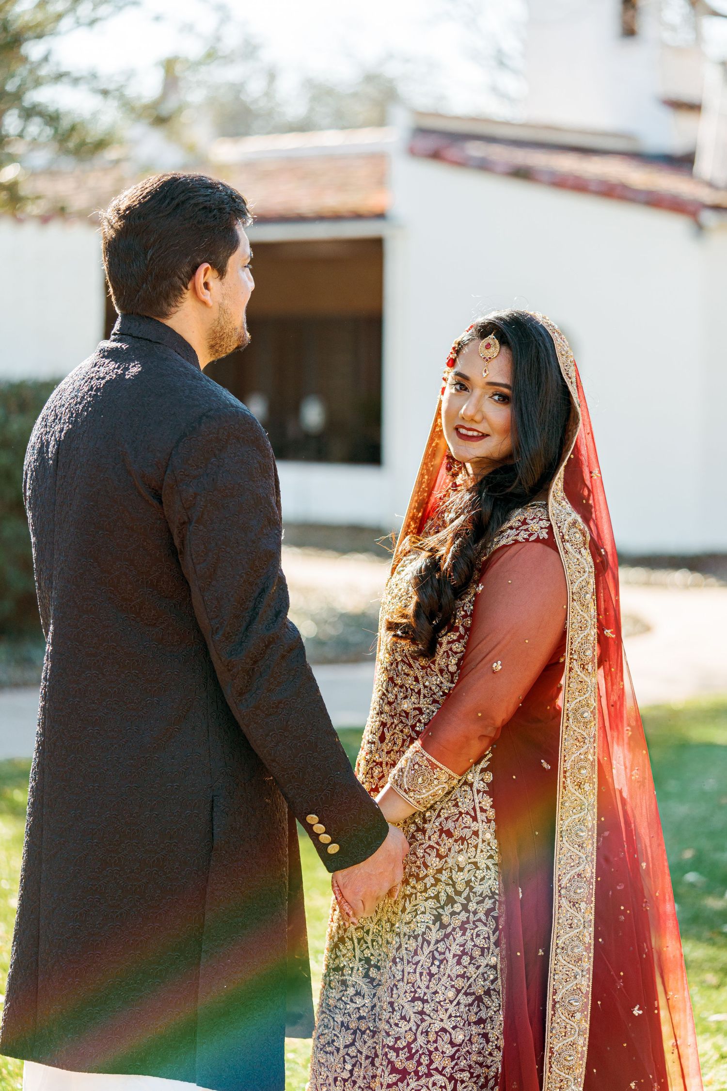 Couple in traditional South Asian wedding attire share candid moments during outdoor photo session.