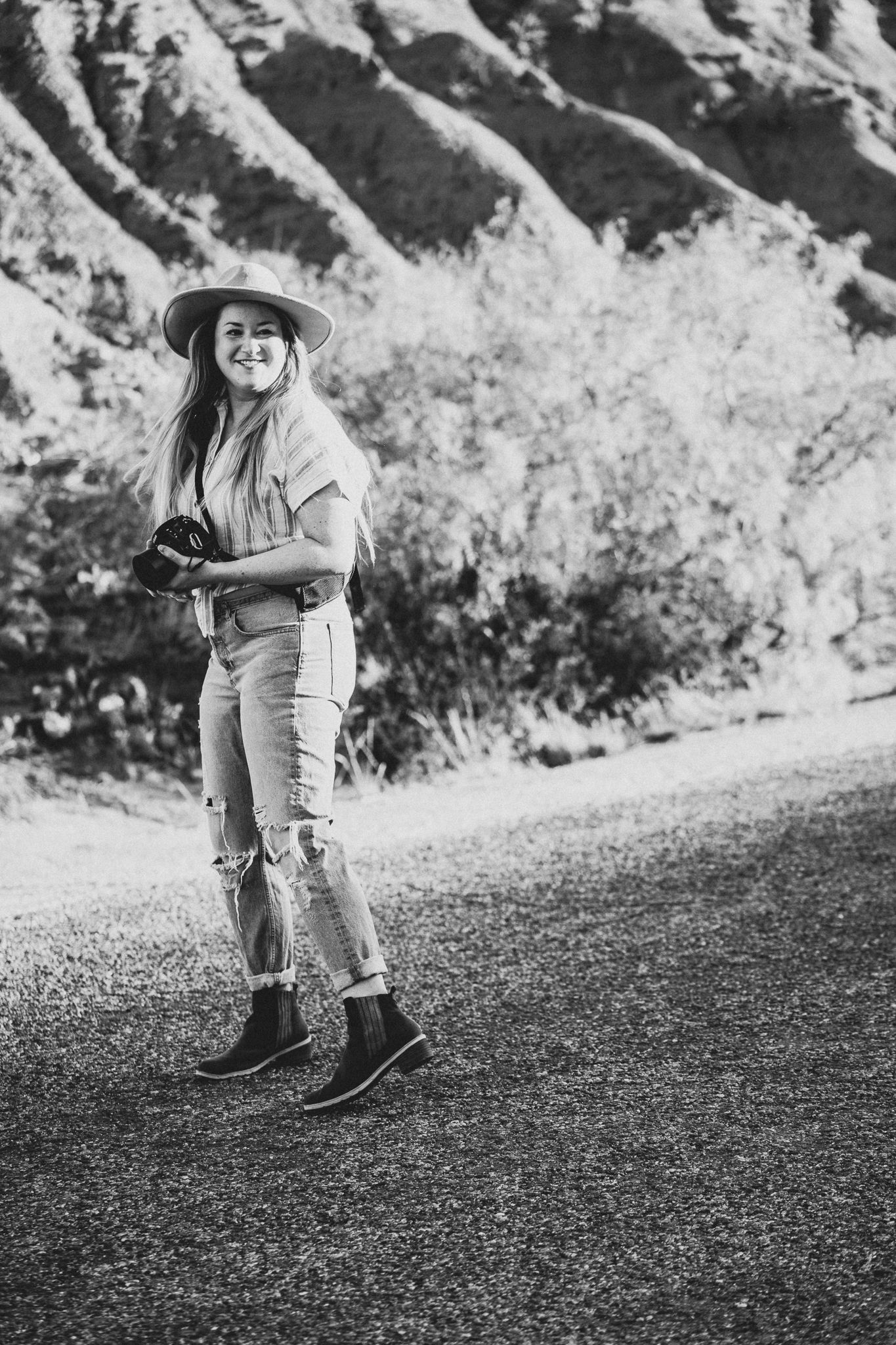 Black and white photo of someone walking on rocky mountain path wearing hiking boots and casual attire.