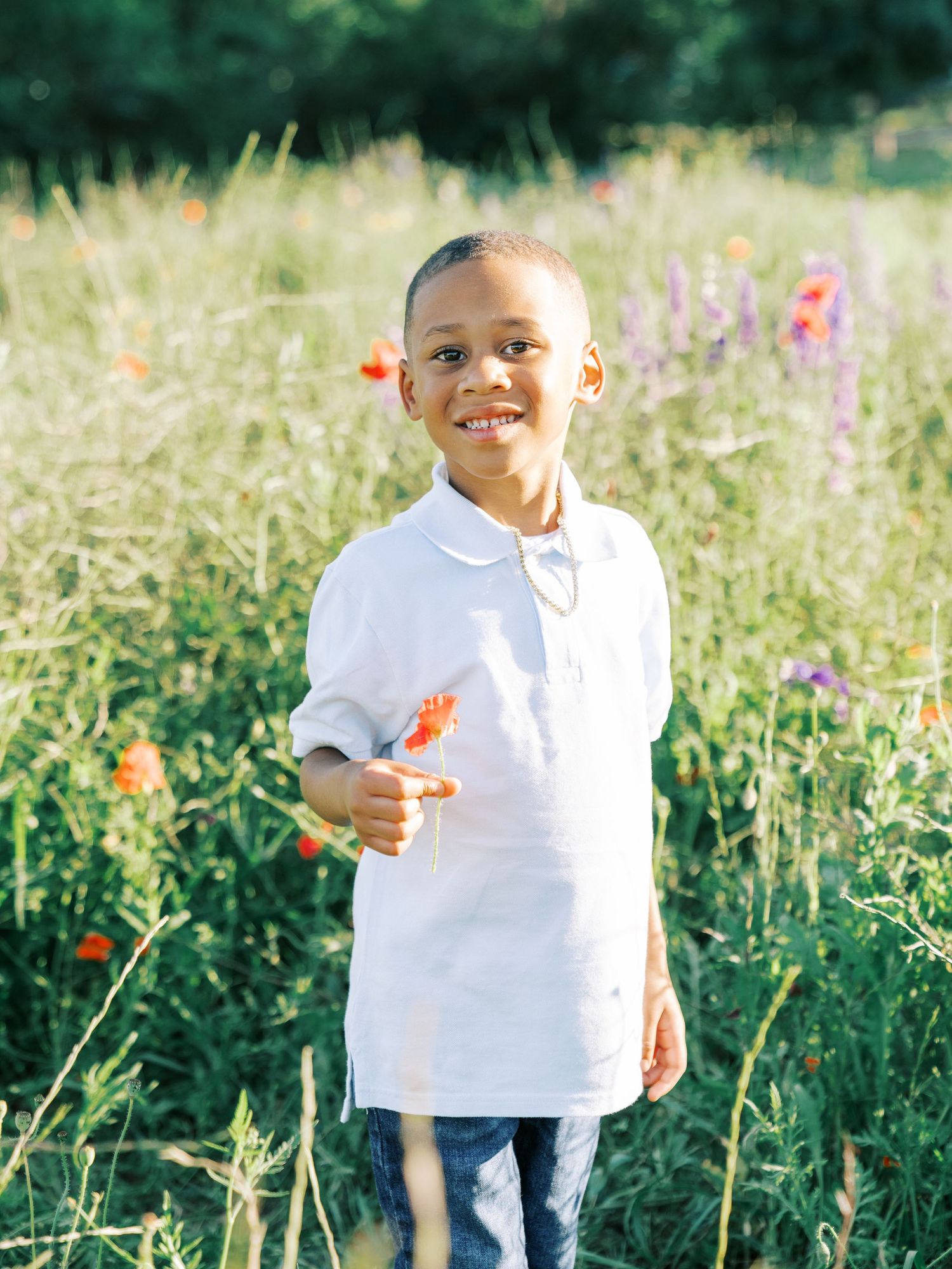 A child wearing a white polo shirt stands in a sunny wildflower meadow with colorful blooms on a summer day.
