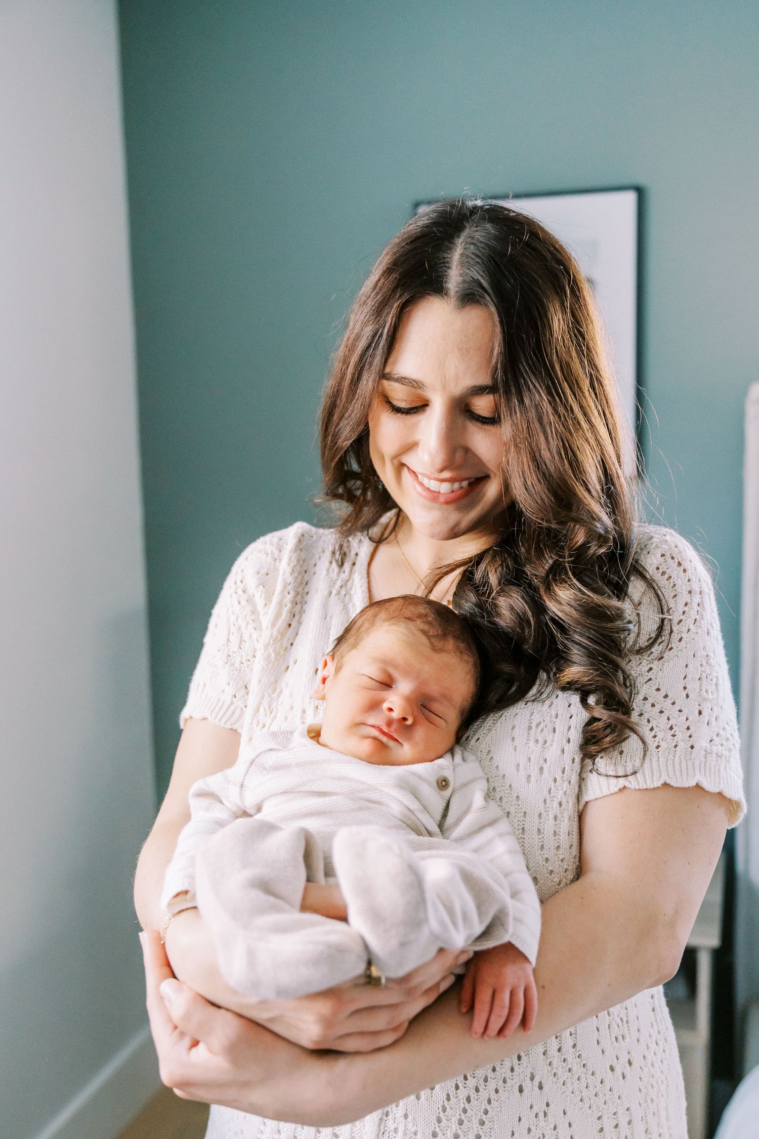 A mother in a white lace dress holds and lovingly gazes at her sleeping newborn baby in a series of tender moments.