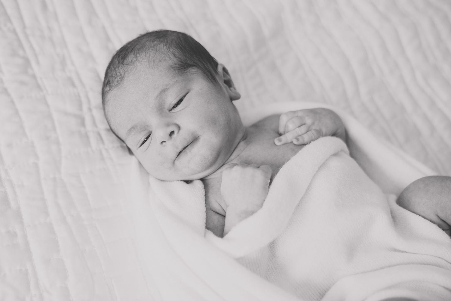 A sleeping newborn baby wrapped in white blankets lies peacefully on soft bedding.