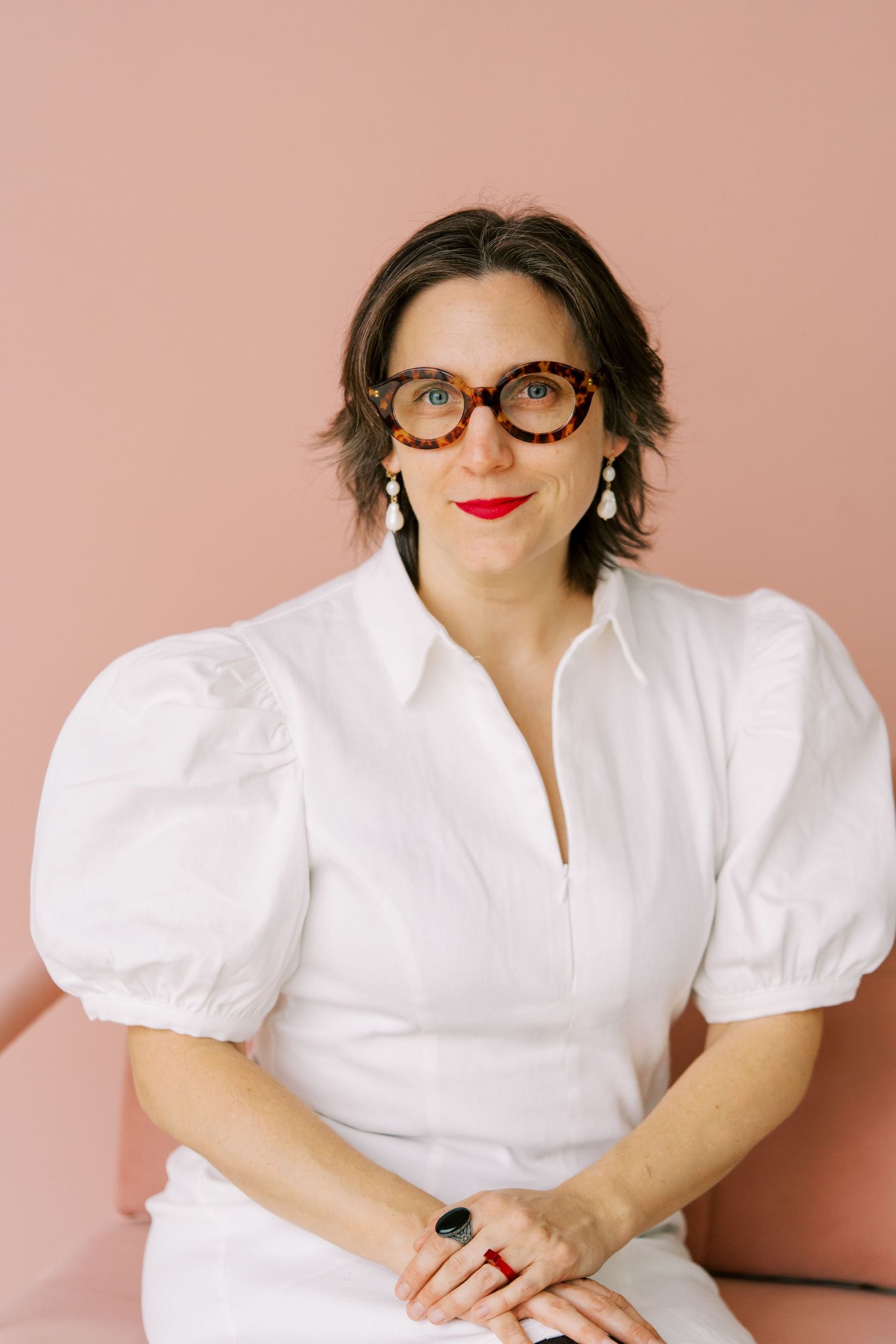Person in white puff sleeve shirt and glasses poses against pink background in a series of casual portraits.