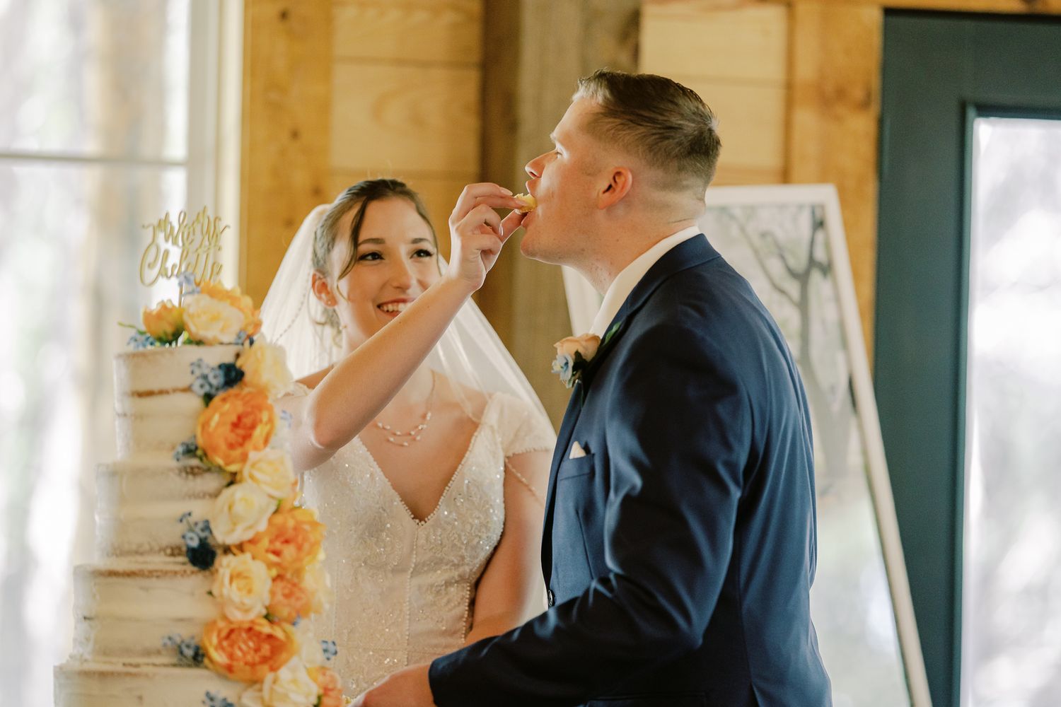 Newlyweds embrace while dancing in a sunlit wooden cabin decorated with peach-colored floral arrangements.