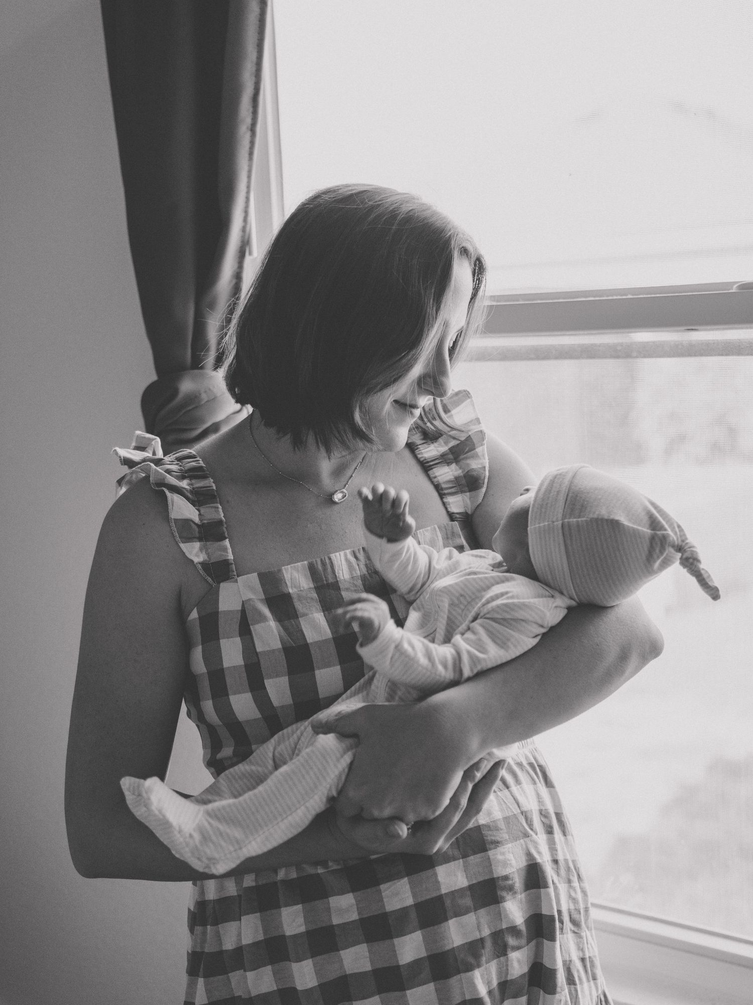A tender moment of parent and newborn bonding in black and white, showing gentle cradling near a window.