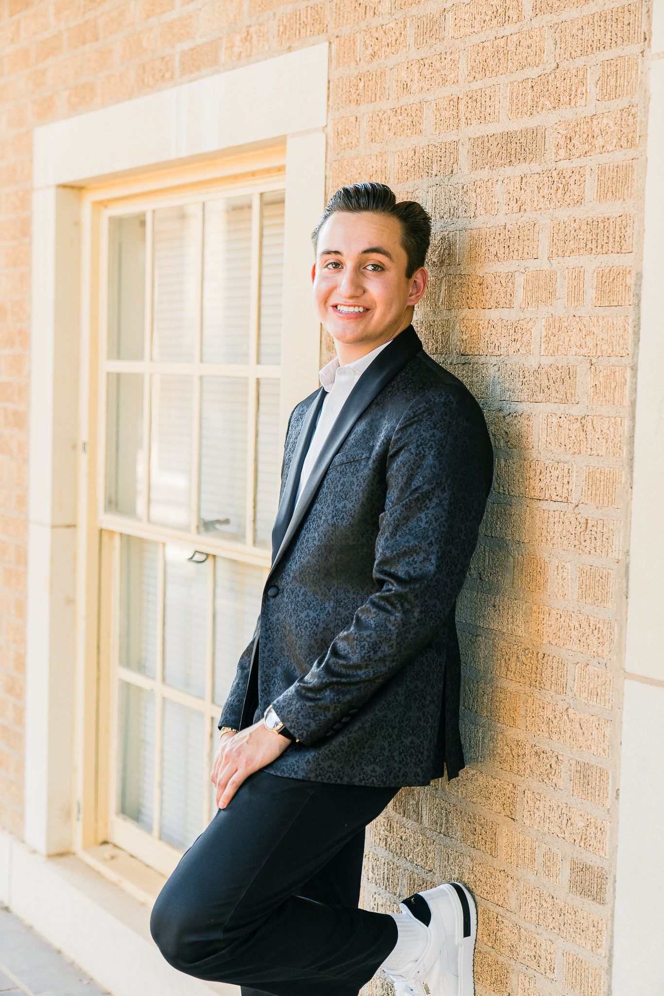 Elegant formal portraits against a beige brick wall featuring a dark textured blazer and white shirt combination.