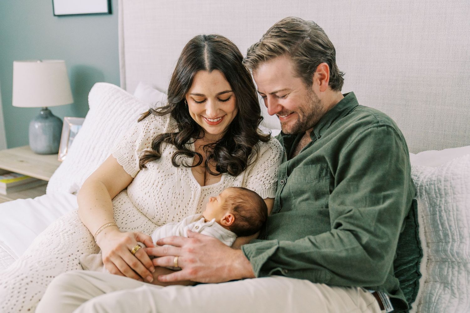 Couple sitting on couch at home while looking at their newborn baby in a tender family moment.