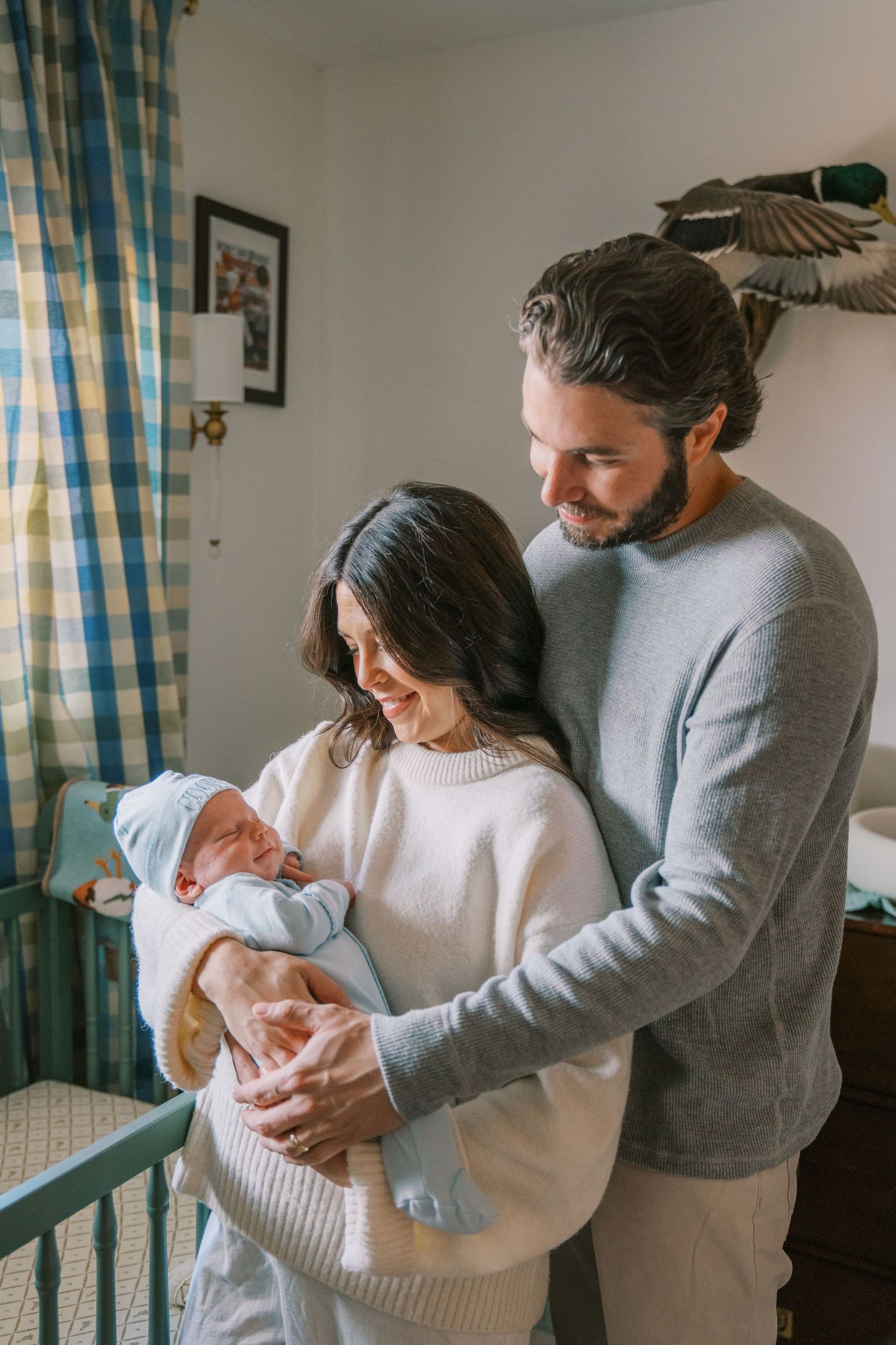 Happy couple admiring their newborn baby in a blue nursery room with plaid curtains.
