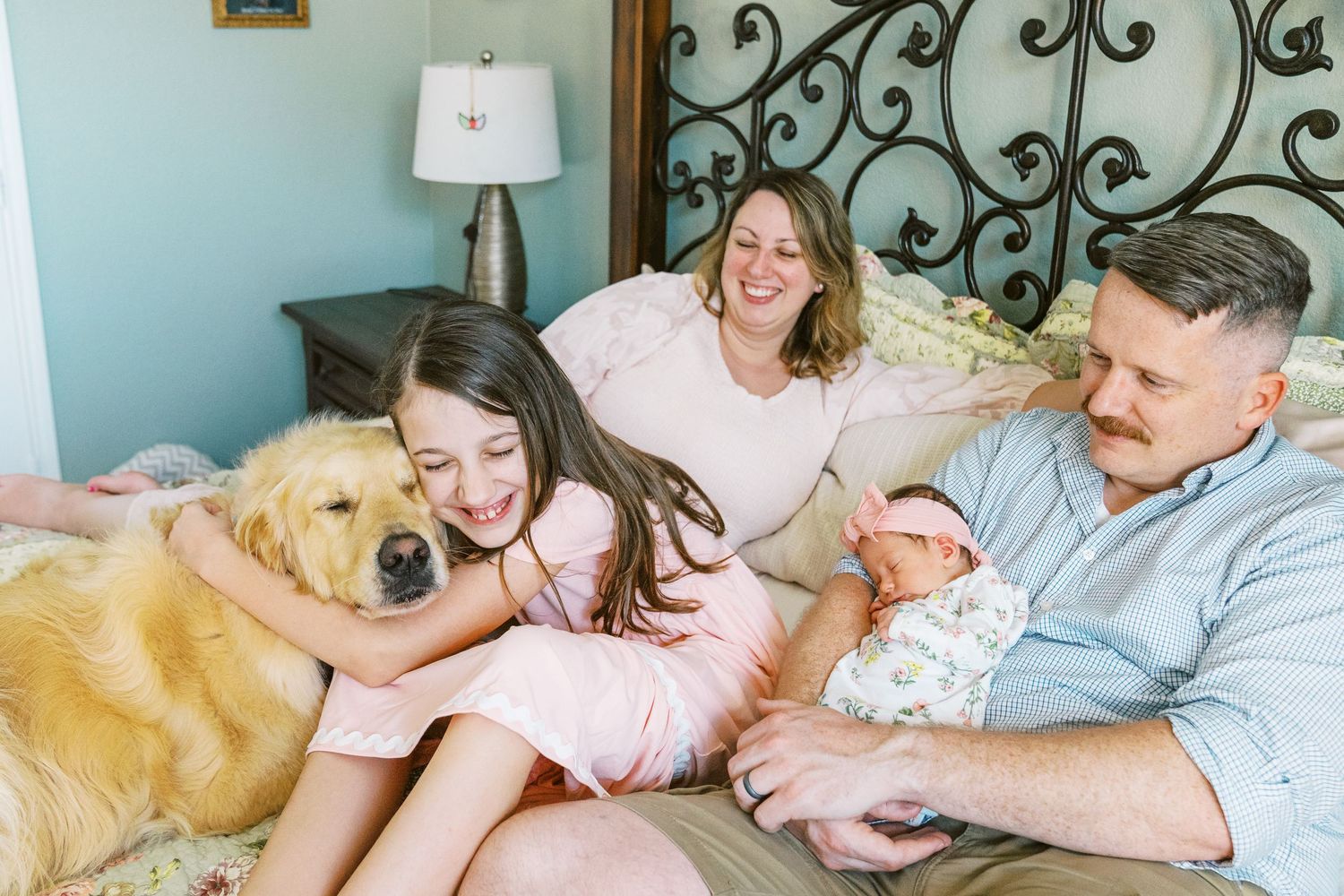 A joyful family moment on bed with golden retriever and sage green walls in background.