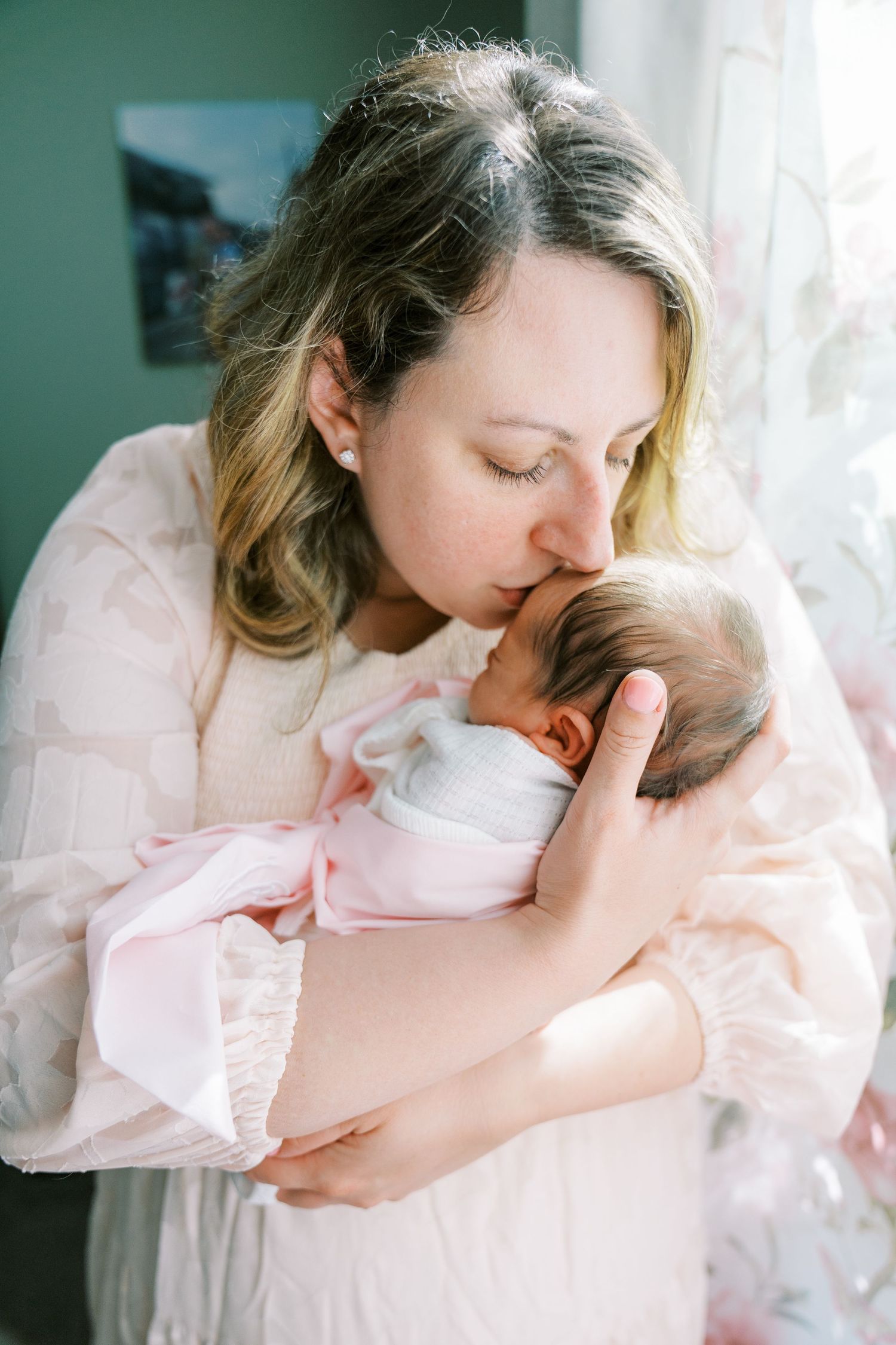 Tender newborn photography session with soft pink and white tones in a sunlit room.