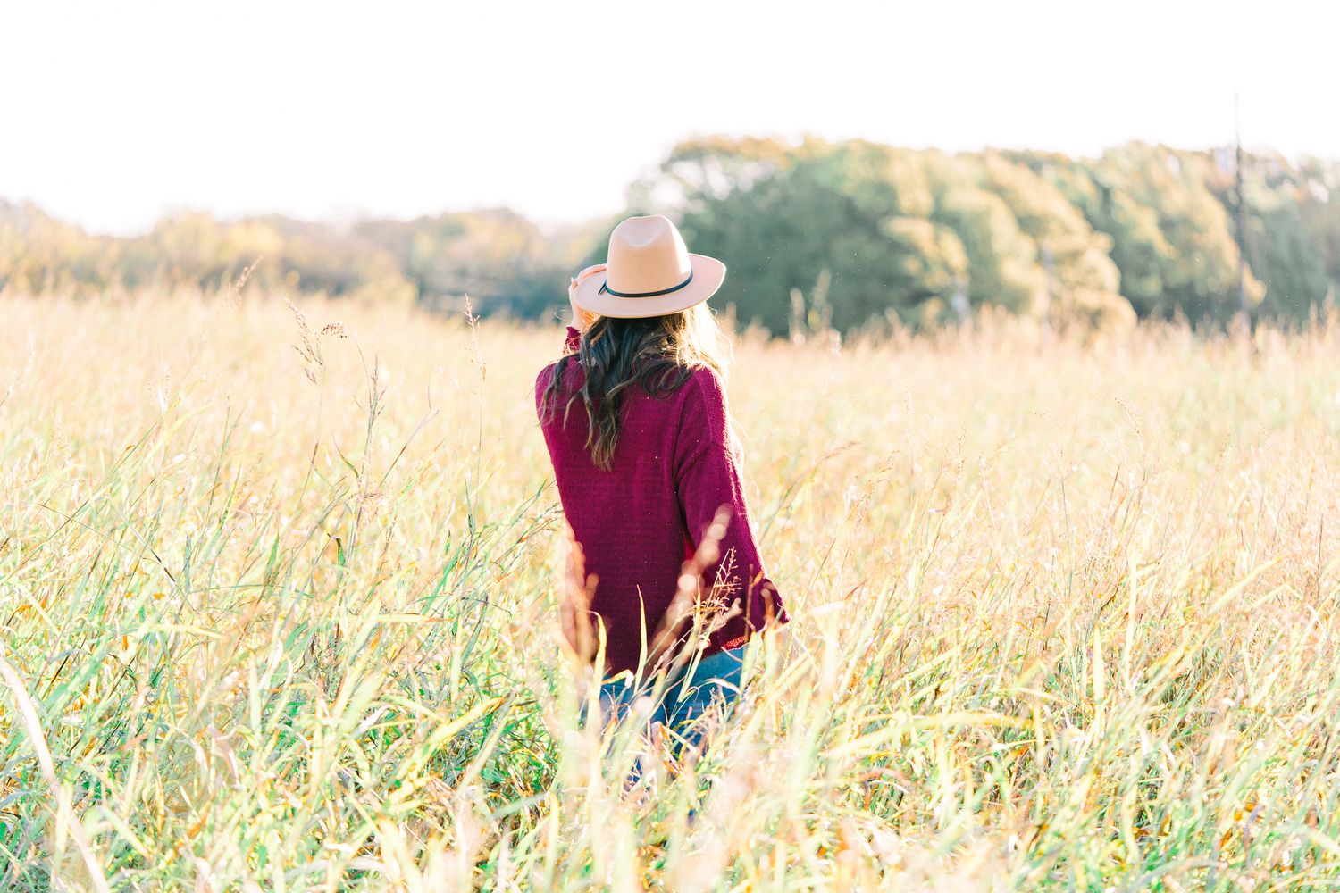 Side view portraits in a rustic field with burgundy sweater and straw hat during sunset.