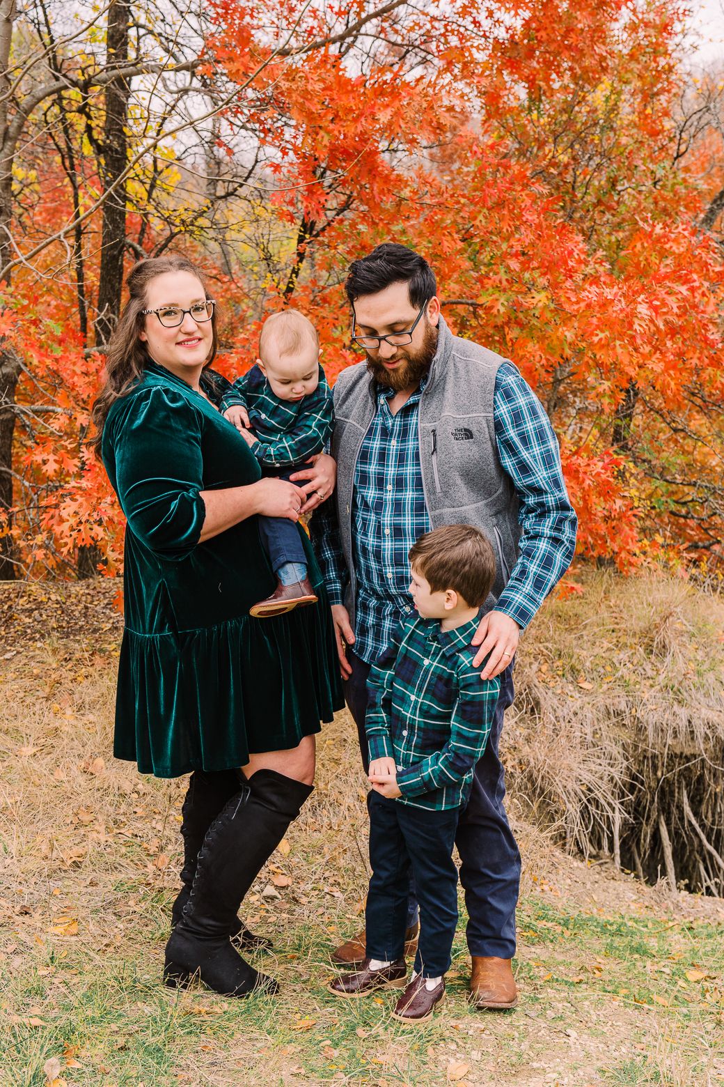Family enjoying playful moments together in a park with bright orange fall leaves in the background.