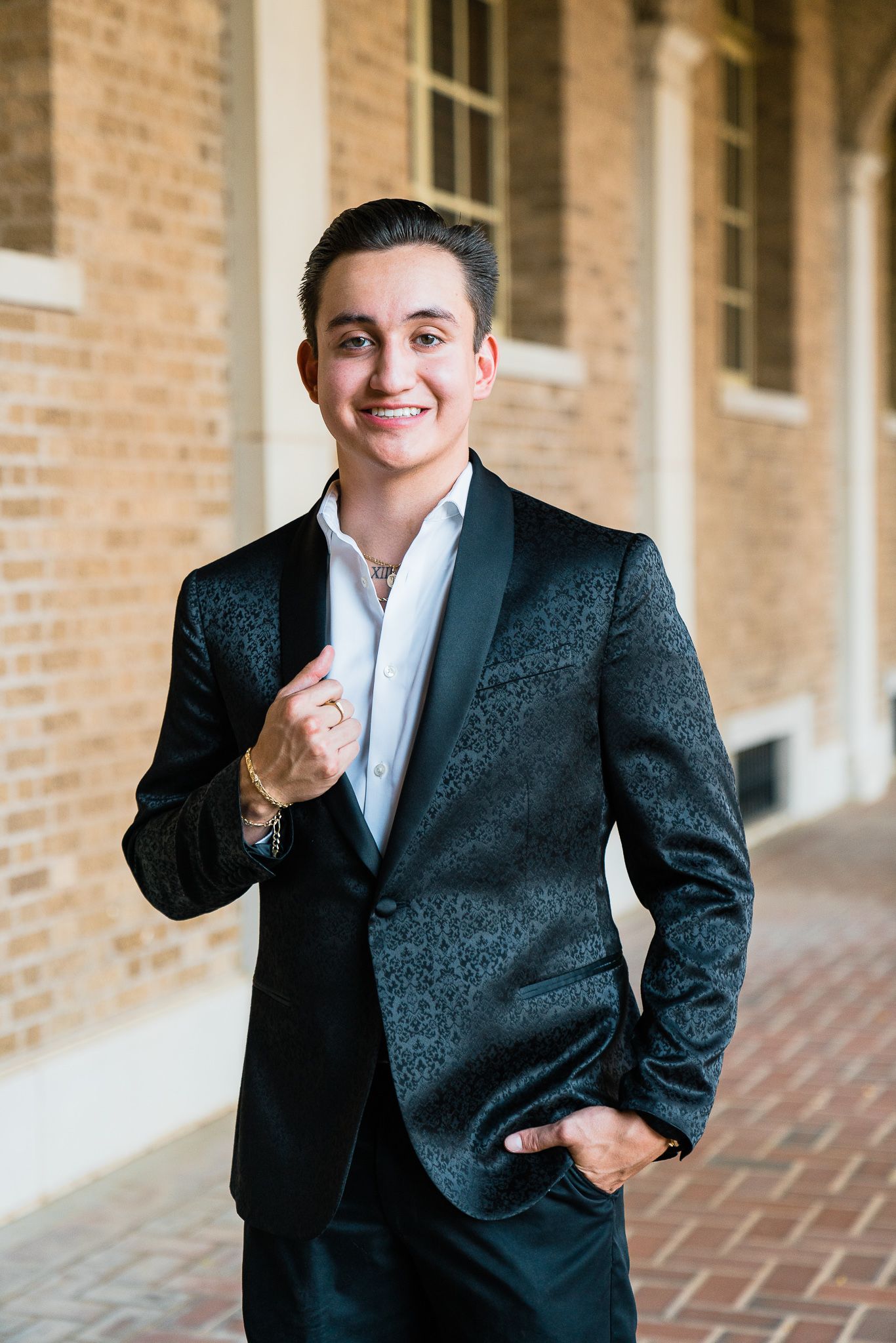 Professional wearing a dark blazer and white shirt poses confidently against a brick wall exterior.