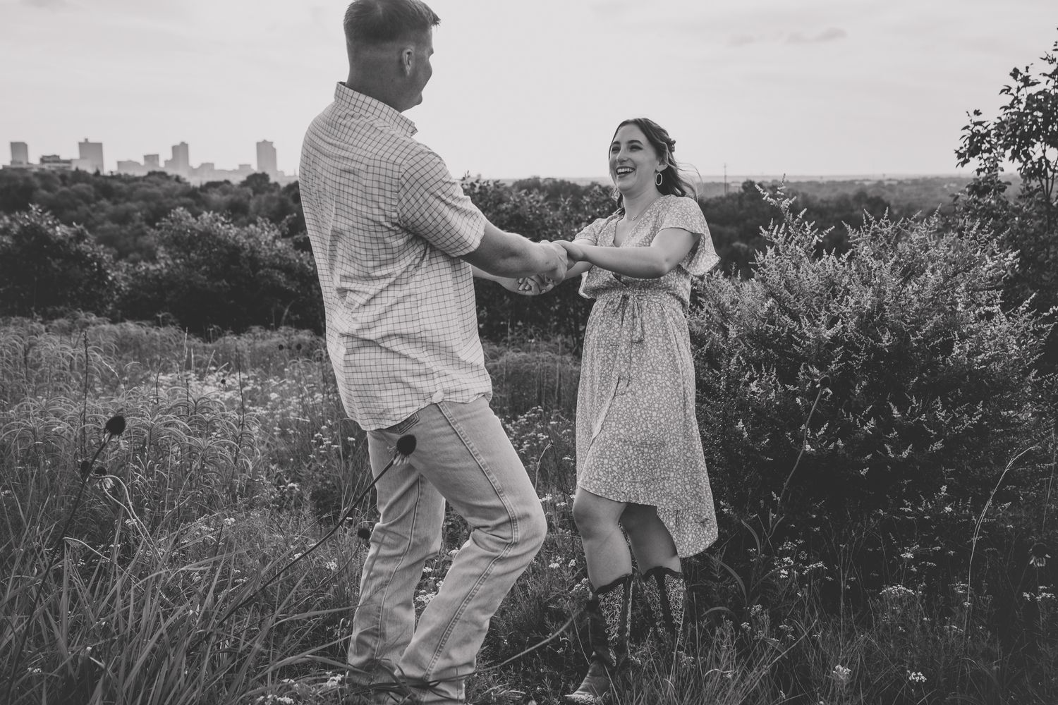 A black and white photo captures a couple dancing together in a natural meadow setting.