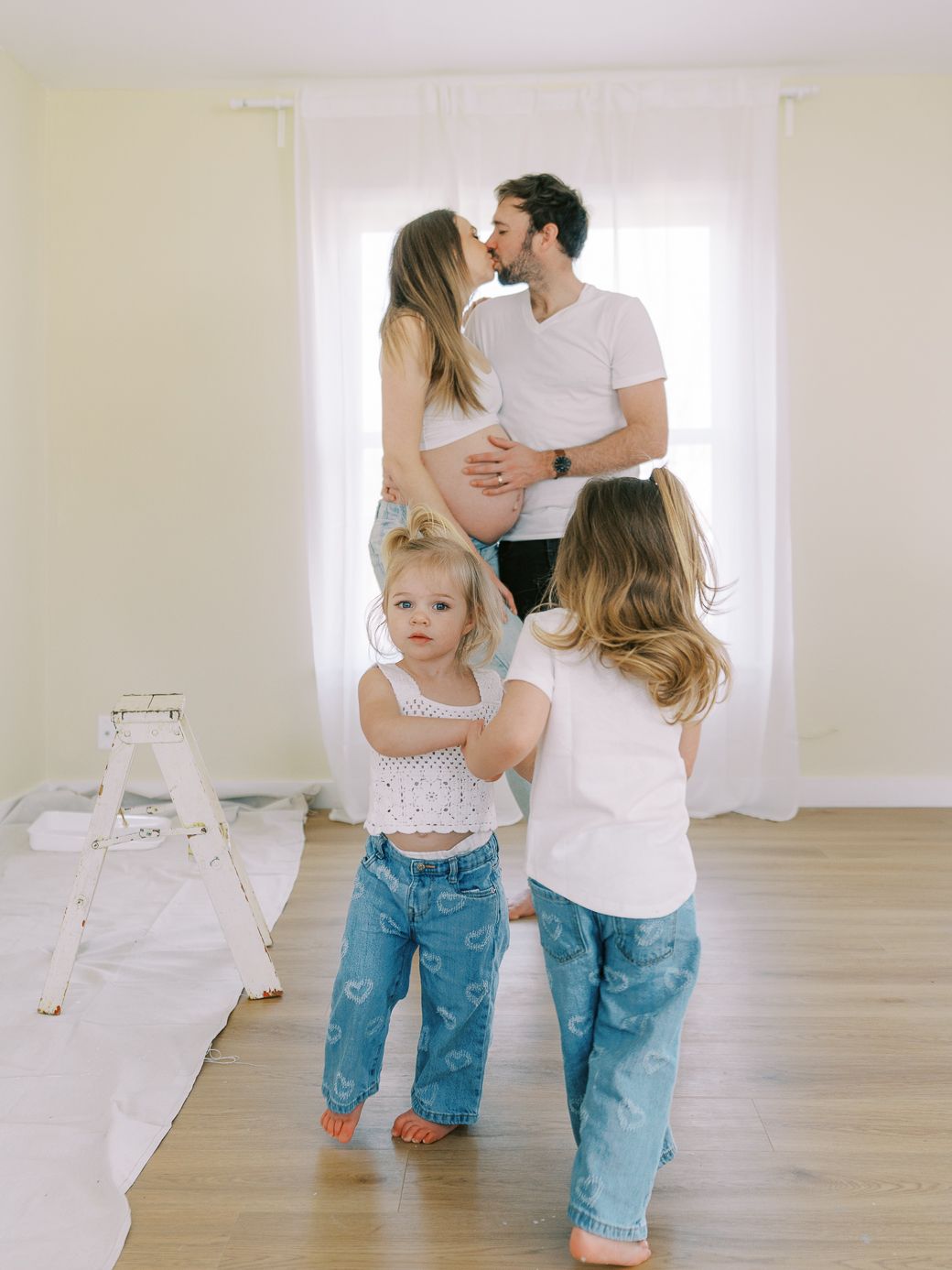 Family painting together in a bright room with white curtains and hardwood floors.