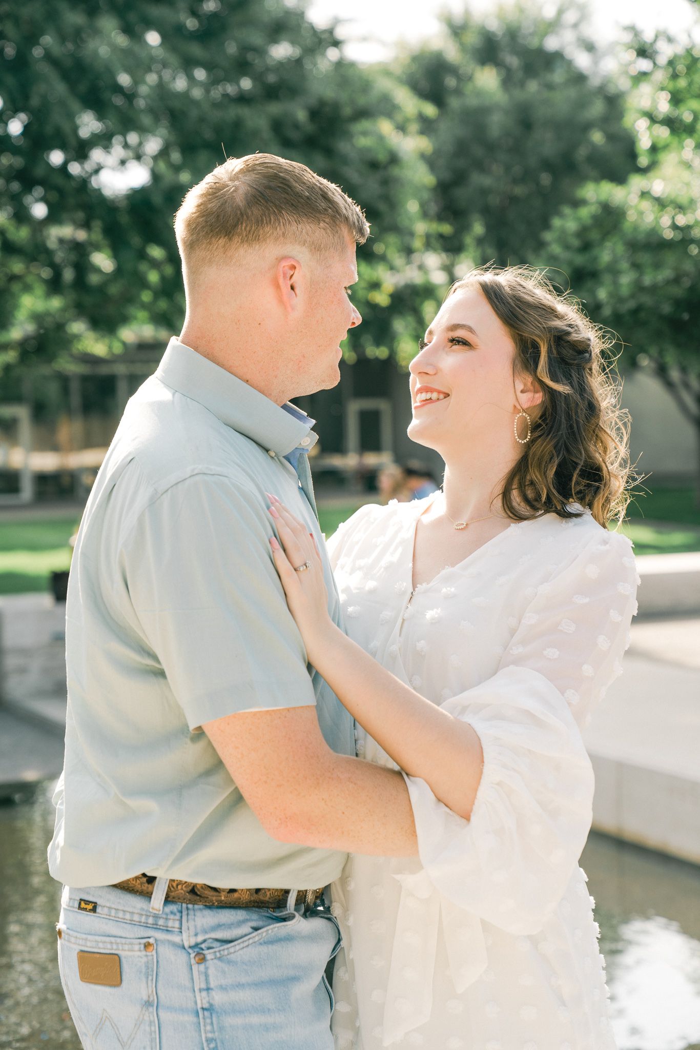 A couple embraces outdoors in a romantic photoshoot near a pond on a sunny day.
