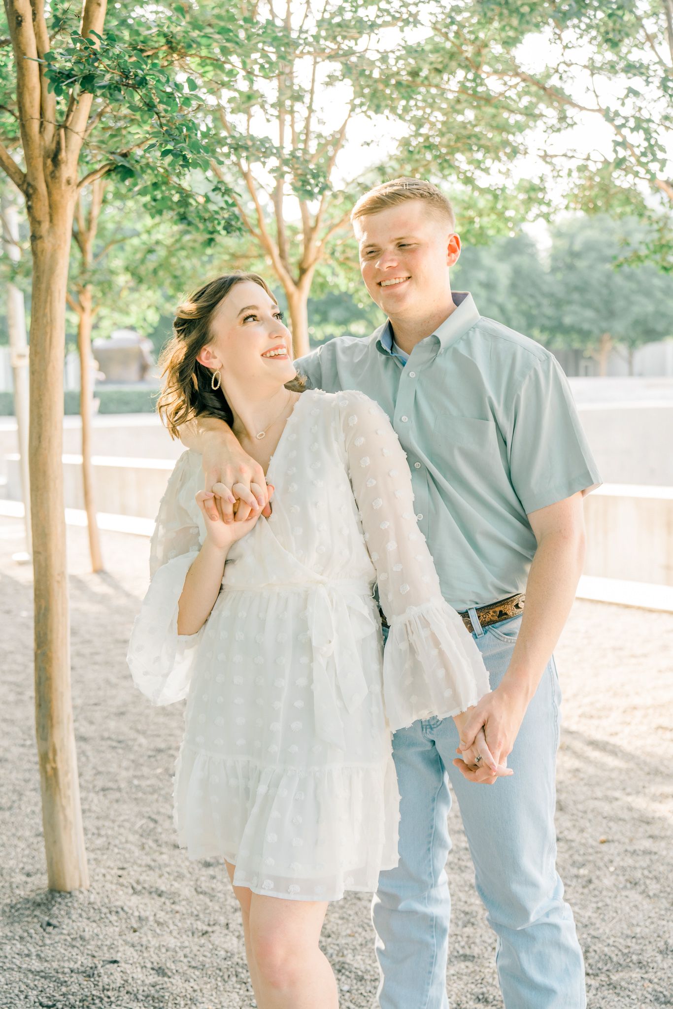 A couple laughs together while holding hands during a sunny outdoor portrait session.