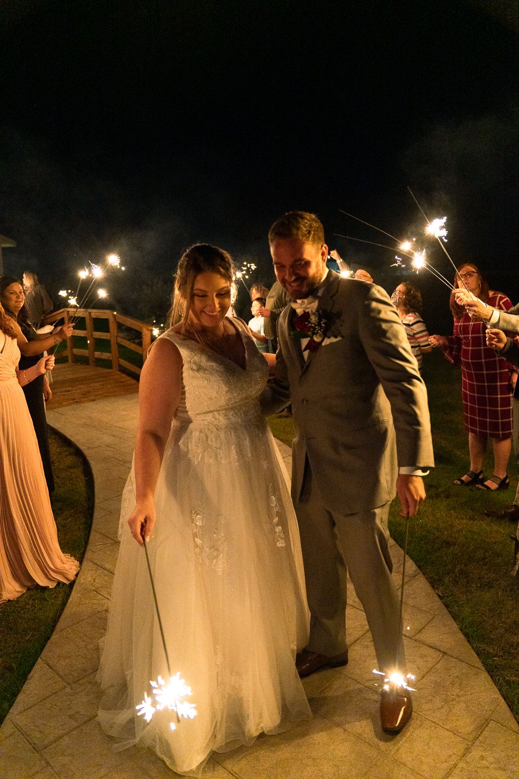 Wedding guests hold sparklers during a nighttime celebration as a couple dances and celebrates on a patio.