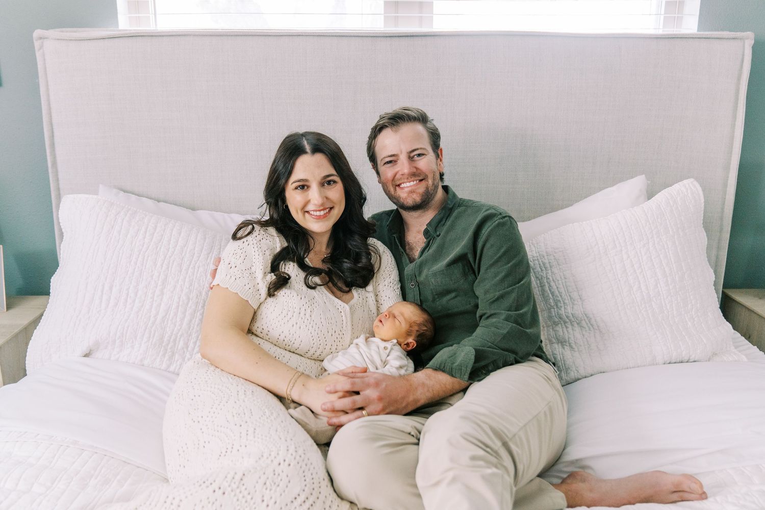 A family lounges together on a white bed while spending quality time at home.