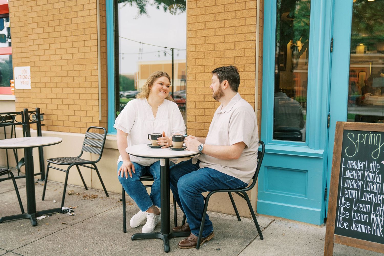 Couple enjoying coffee and conversation at an outdoor cafe table beside a colorful storefront.