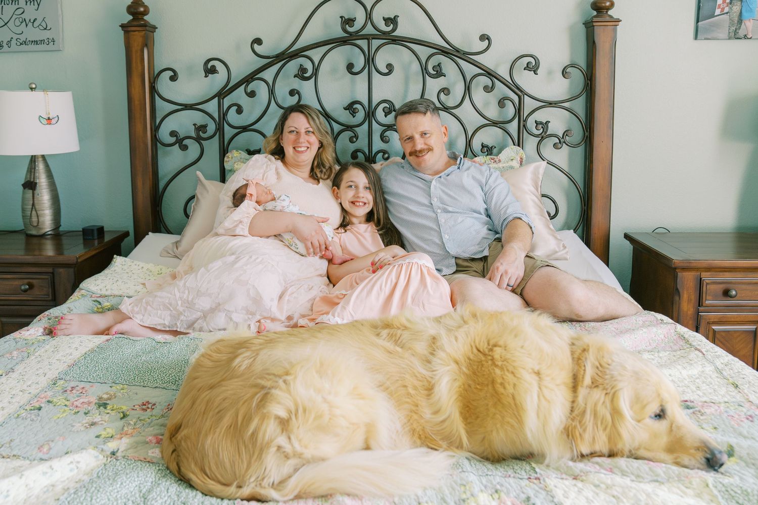 Family relaxes on white bedding with golden retriever dogs.