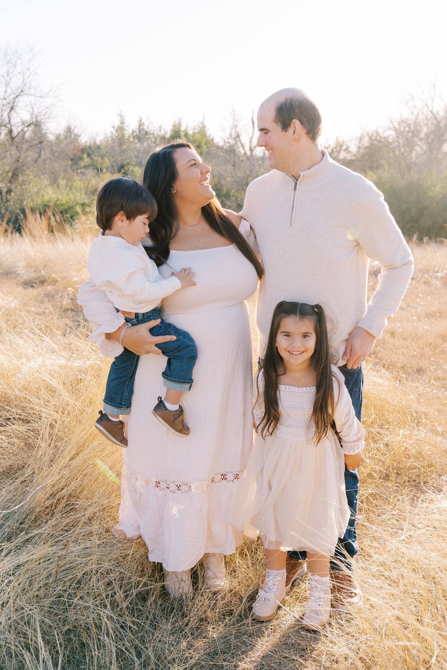 Family in white outfits poses together in golden field during sunset photoshoot.