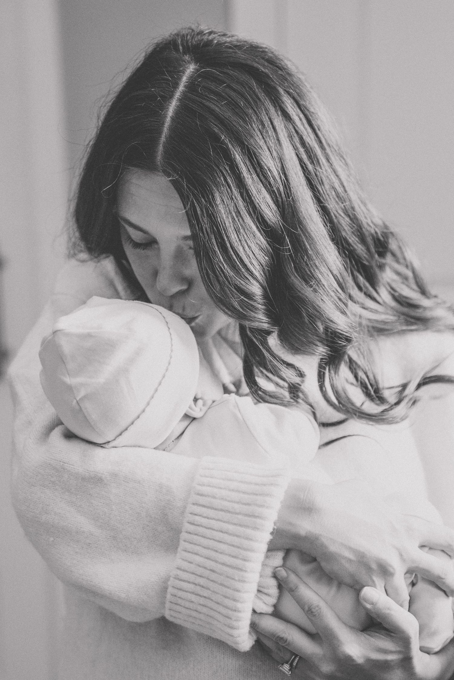 Black and white photo of a mother tenderly holding her newborn baby wrapped in white blanket and hat.
